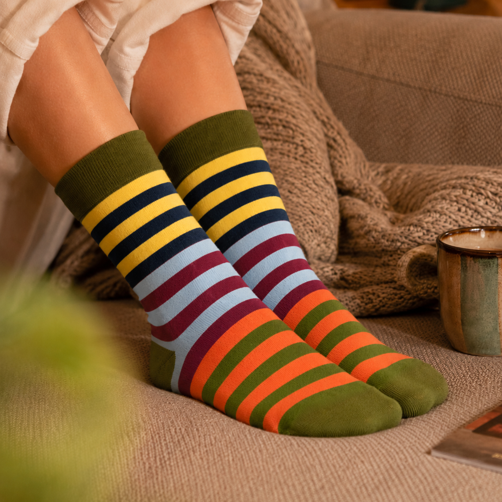 Gestreifte Socken mit buntem Muster aus horizontalen Streifen. Farben: Olivgrün am Bund, an Ferse und Spitze; dazu Gelb, Dunkelblau, Hellblau, Burgunderrot und Orange am Bein. Weich, dehnbar, Gr. 41-46.