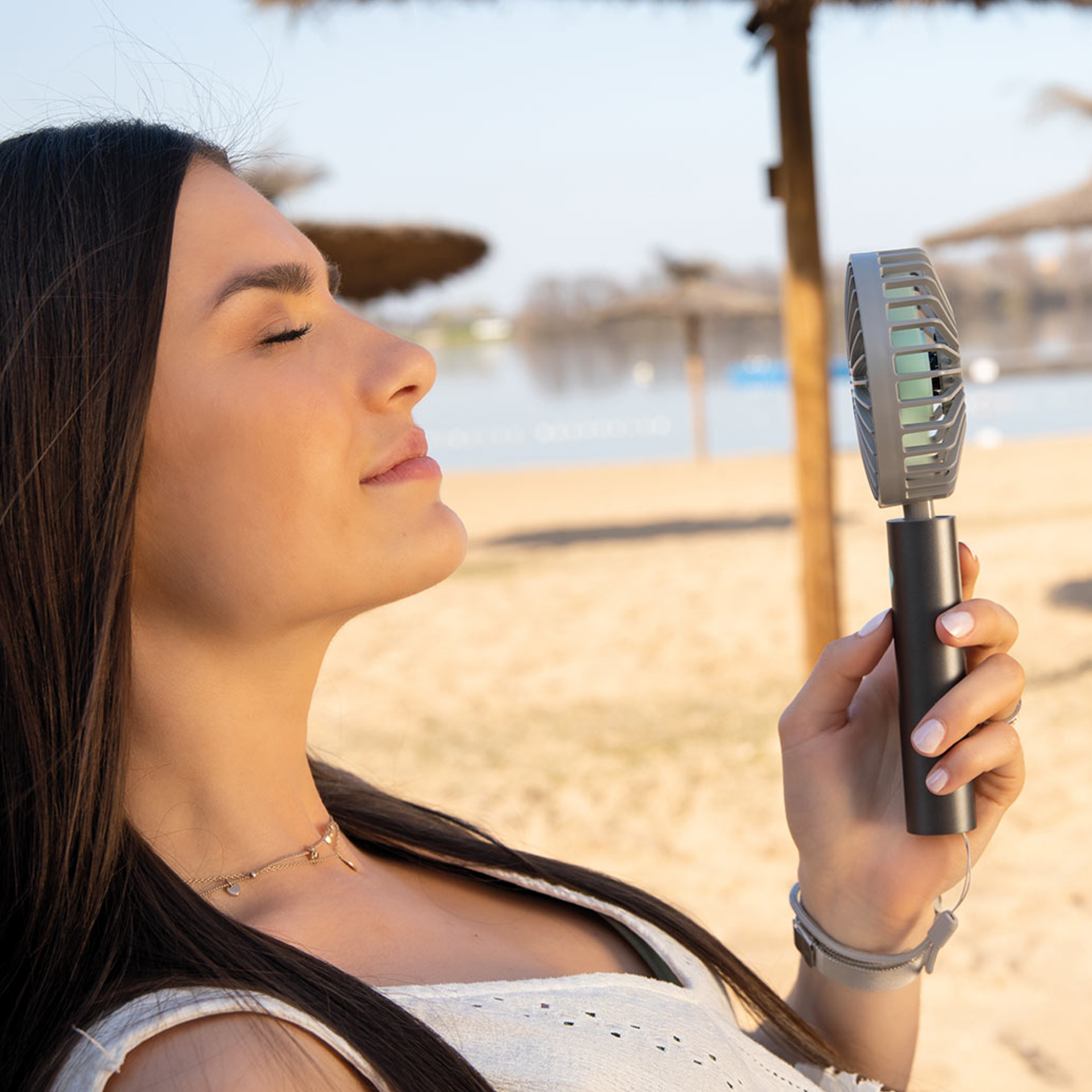 Une femme profite de la brise d'un ventilateur Flow de couleur graphite sur la plage, les yeux fermés.
