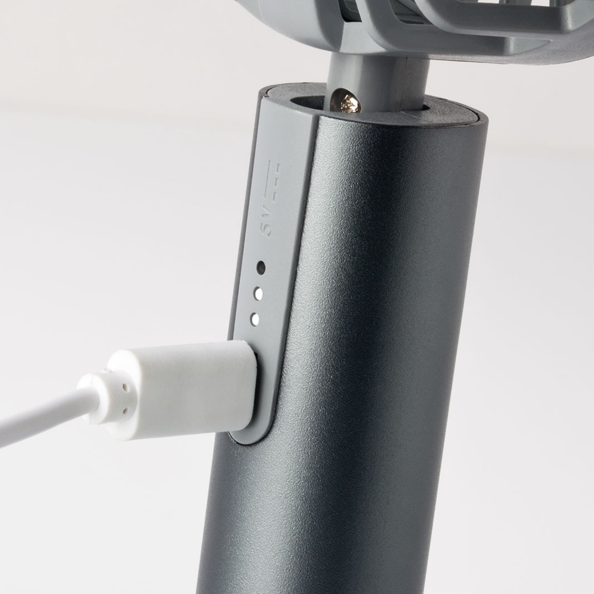 Vue détaillée du ventilateur Flow 'graphite' : le câble USB est inséré dans le boîtier gris du ventilateur à batterie, à côté de l'indicateur de charge de la batterie.