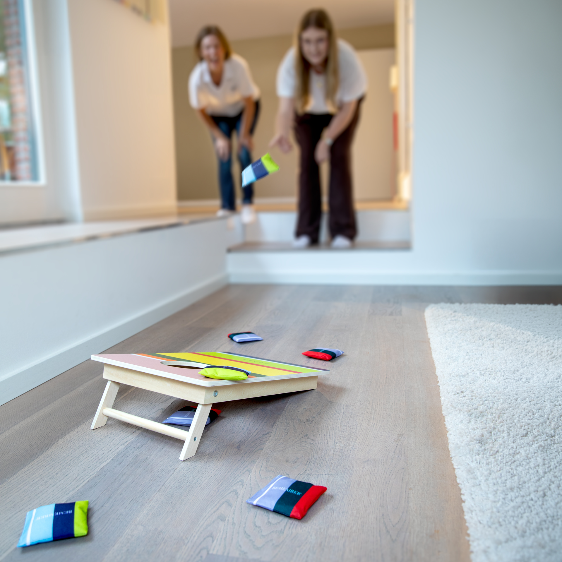 Un plateau de jeu Cornhole avec des cases colorées et un trou, entouré de petits sacs à lancer de différentes couleurs.