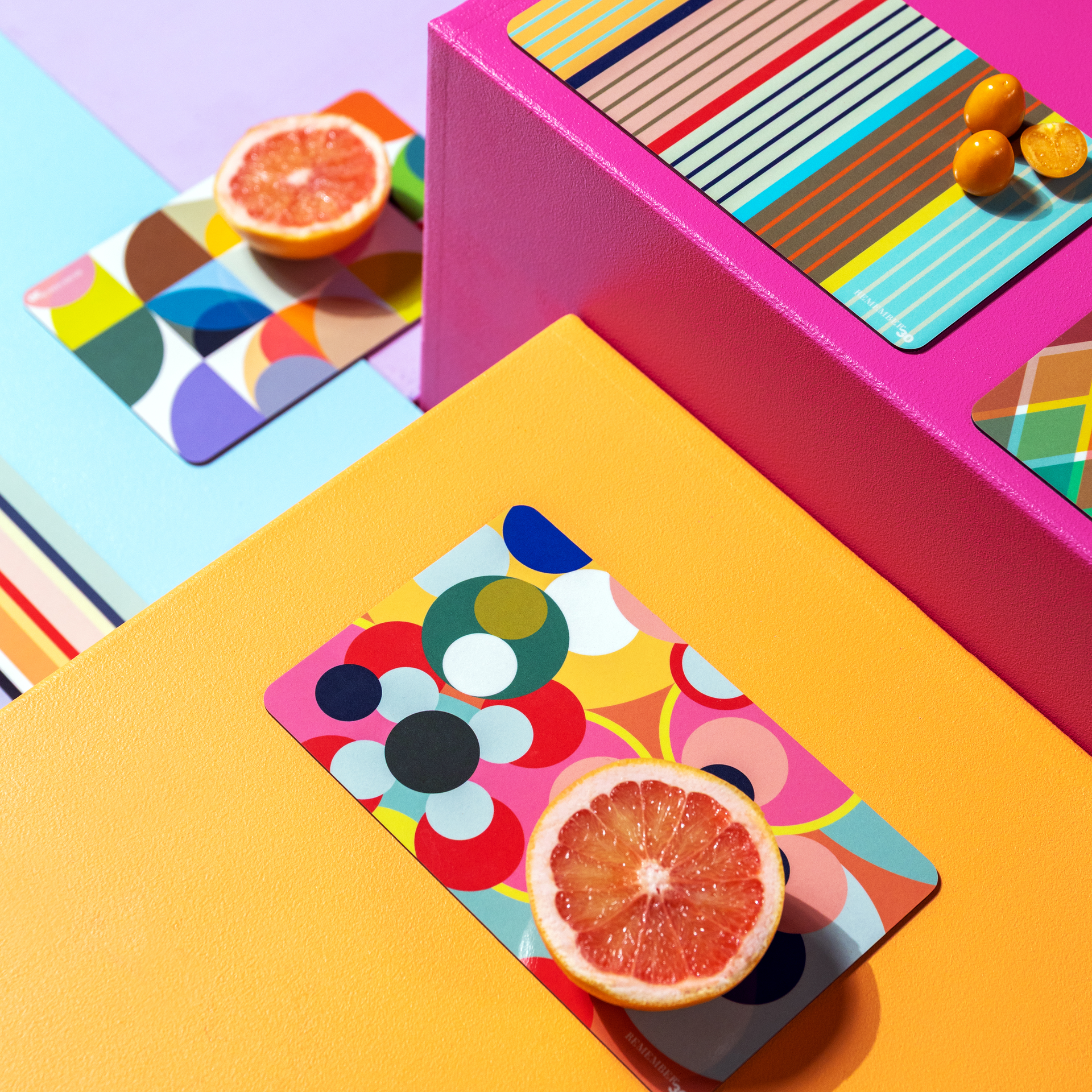 Abstrakte Komposition aus farbigen Blöcken, Karten mit Mustern und Frucht-Hälften. Lebendige Farben und geometrische Formen dominieren. Grapefruit und Kumquats liegen auf den Karten.