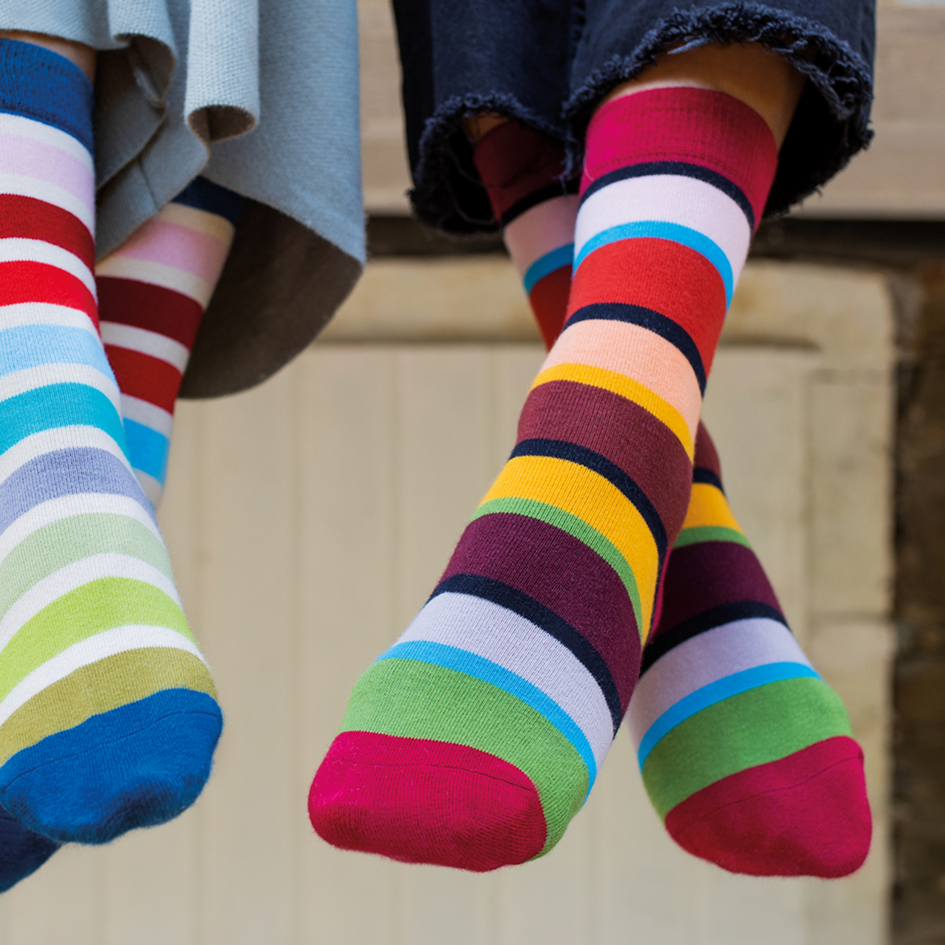 Dos unidades de calcetines de rayas de colores en tallas 36-41. Los calcetines son muy suaves y cálidos. Una persona lleva vaqueros azules y la otra, una falda gris.
