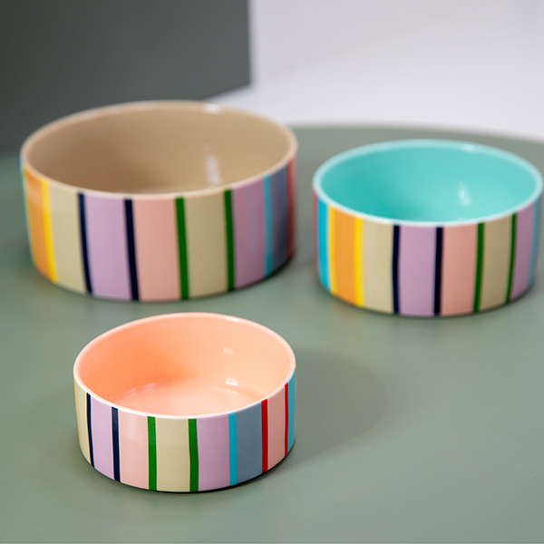 Three round ceramic bowls in various sizes with a light green finish. Each features vibrant vertical stripes on the outside in pink, purple, blue, green, yellow and orange. The inside is in pastel shades: beige, turquoise and peach.