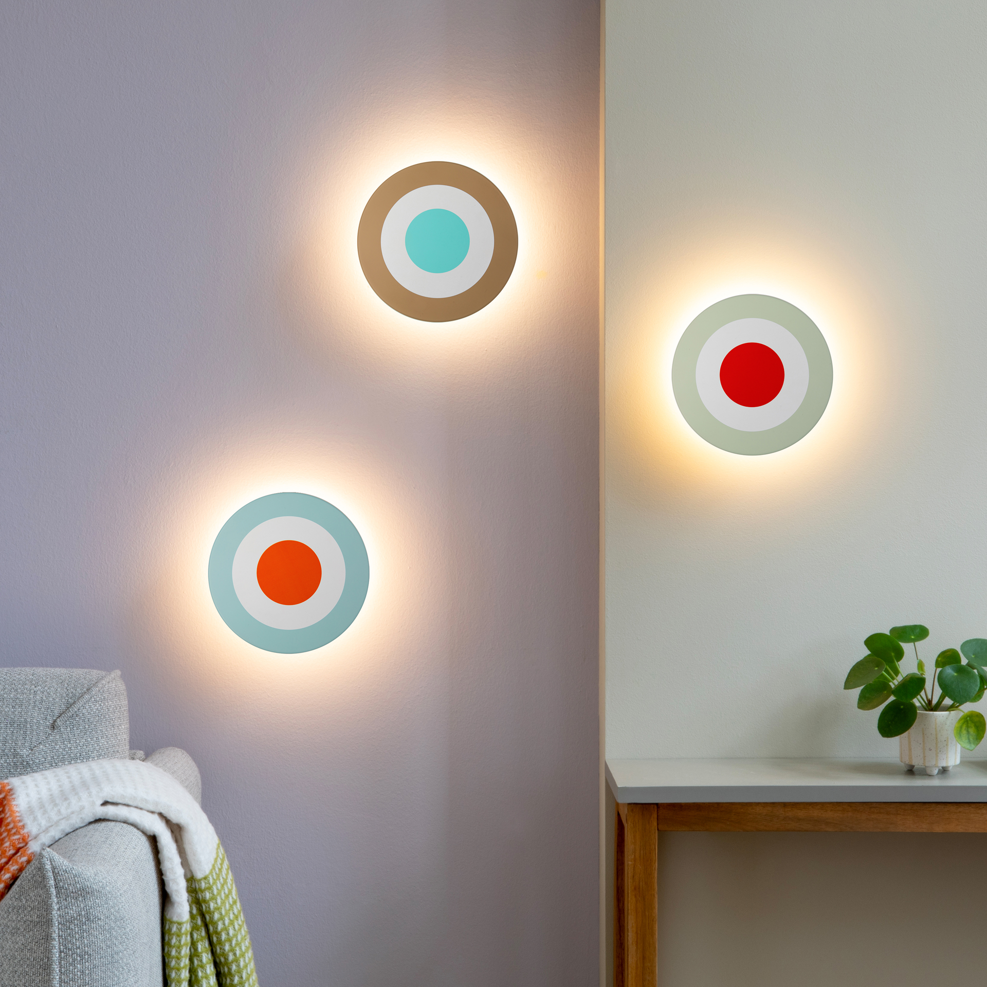 Runde, moderne Wandleuchte mit hellblauem Außenring, weißem Mittelring und leuchtend orangefarbenem Punkt im Zentrum. Das schlichte Kreisdesign der DOT Wandleuchte hebt sich plastisch vom weißen Hintergrund ab.
