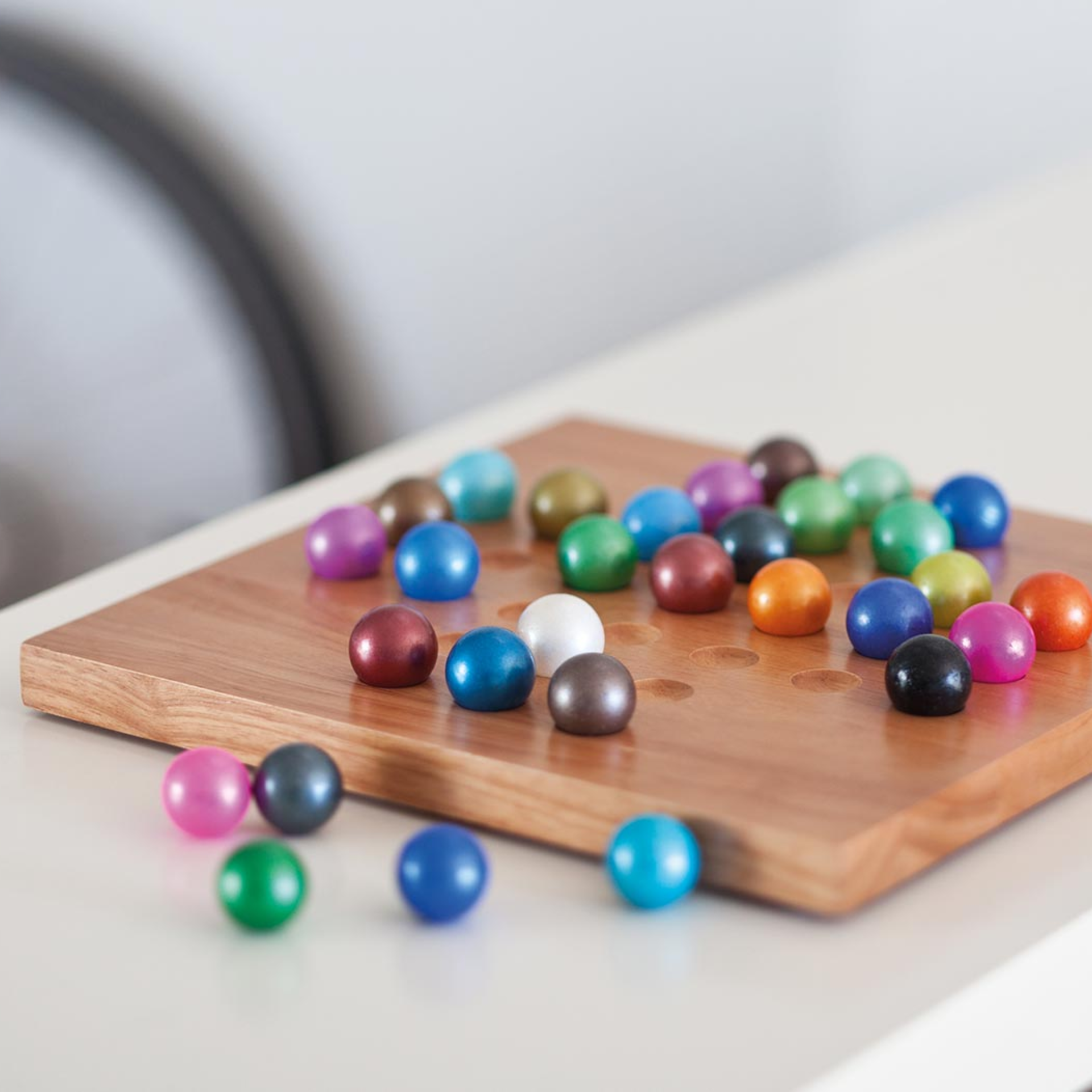 Wooden board with hollows, coloured glass balls lying on it, some also scattered outside the board. Solitaire game.