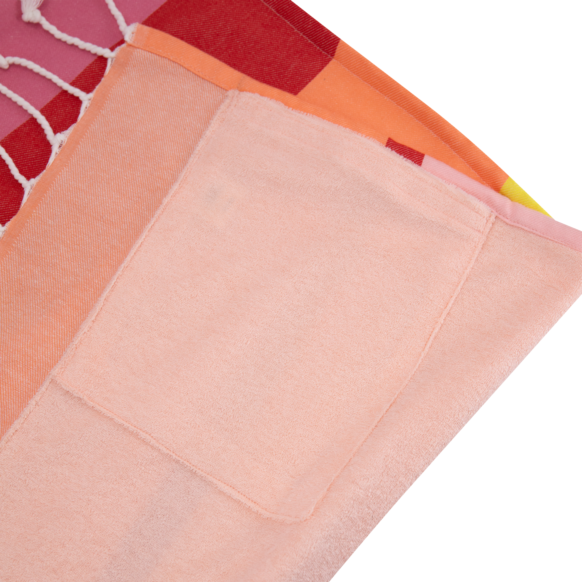 Un morceau de tissu coloré et plié avec des franges, composé d'éléments à carreaux rouges et oranges et d'un foulard uni de couleur pêche claire avec une poche cousue dessus.