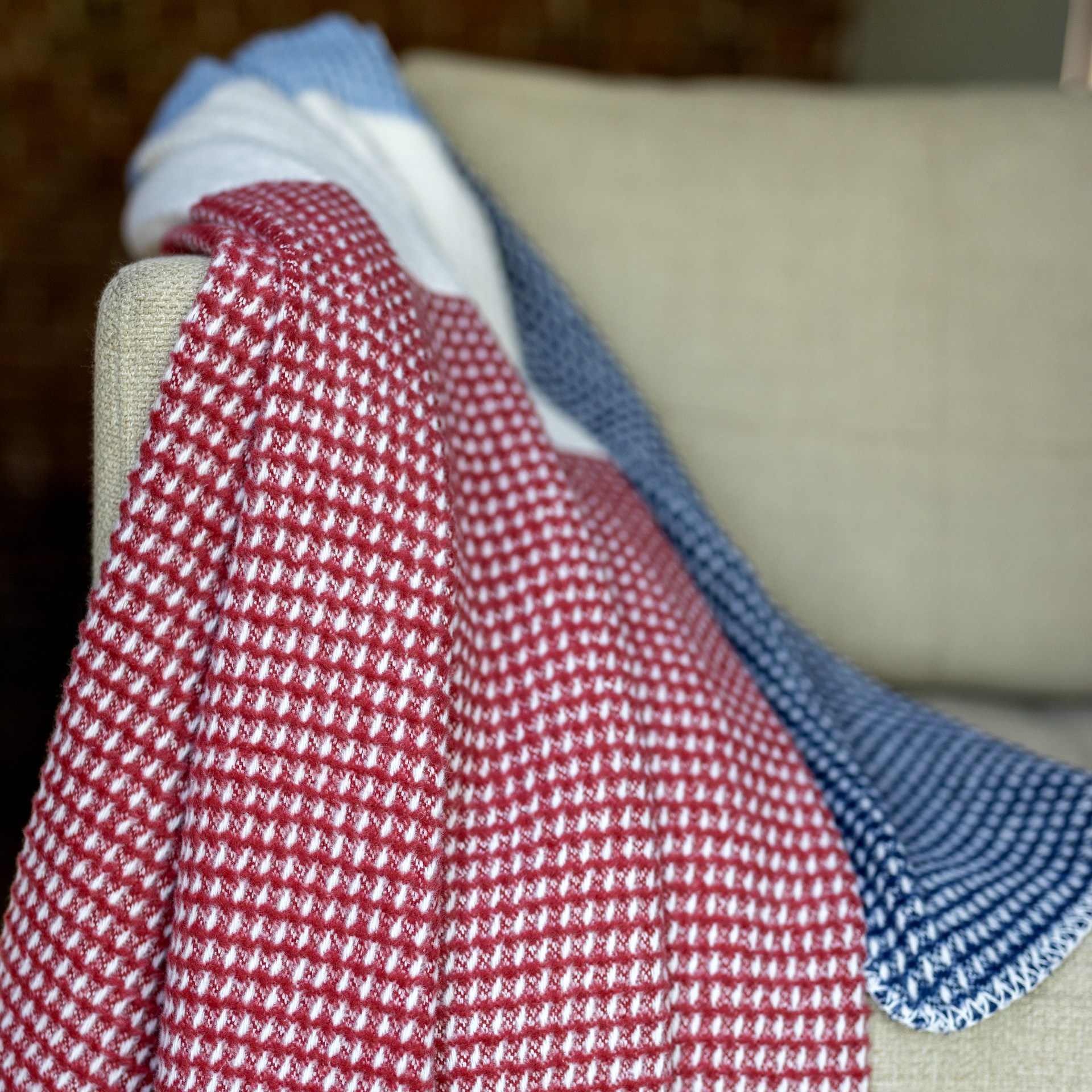 Detalle de una manta para sofá «Malie» en rojo, blanco y azul con diseño de rombos, colocada sobre un sofá.