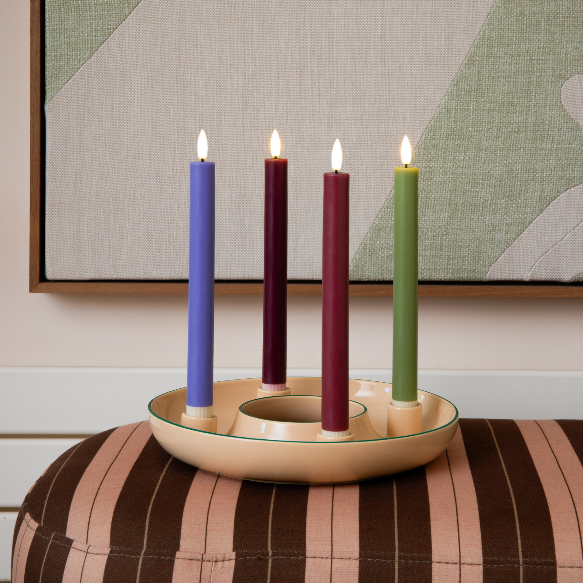 Runde, beige Kerzenschale „Lucia“ aus Dolomit-Keramik mit vier Halterungen für Stabkerzen. Vier zweifarbige Kerzen: mintgrün-rot, mintgrün-dunkelrot, orange-blau, olivgrün-limettengrün. Warmes Deko-Element.