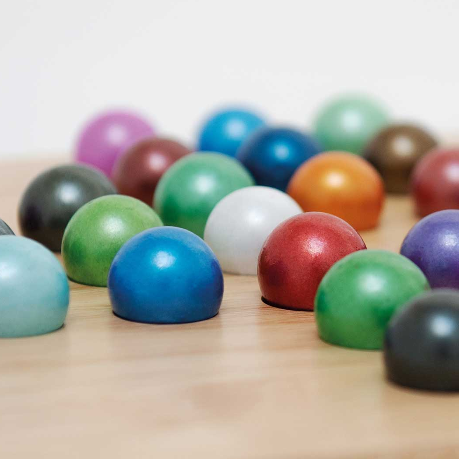Close-up of colourful glass balls from the solitaire game on a light-coloured wooden background. The balls shimmer in different colours.