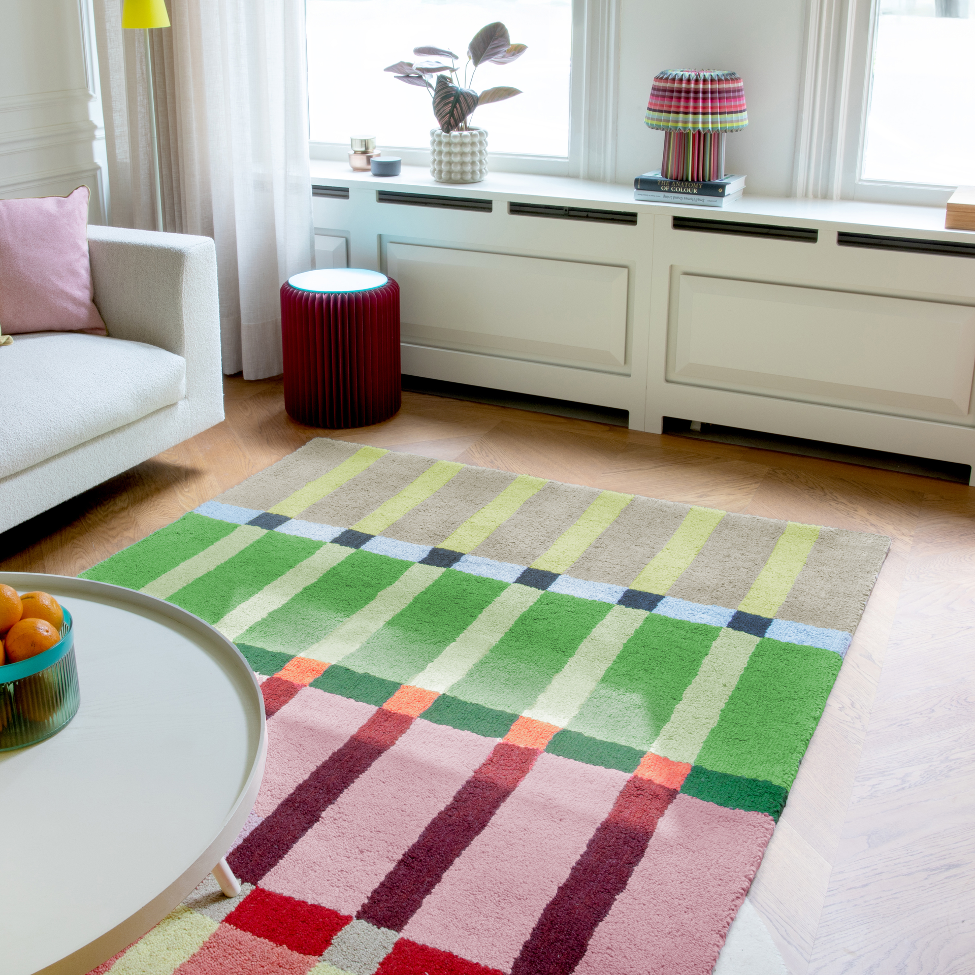 Alfombra rectangular «Kaido» con un diseño de rayas multicolor en tonos beige, verde, rosa y rojo. Las rayas se disponen de forma horizontal. Los detalles de color verticales unen las zonas de color.