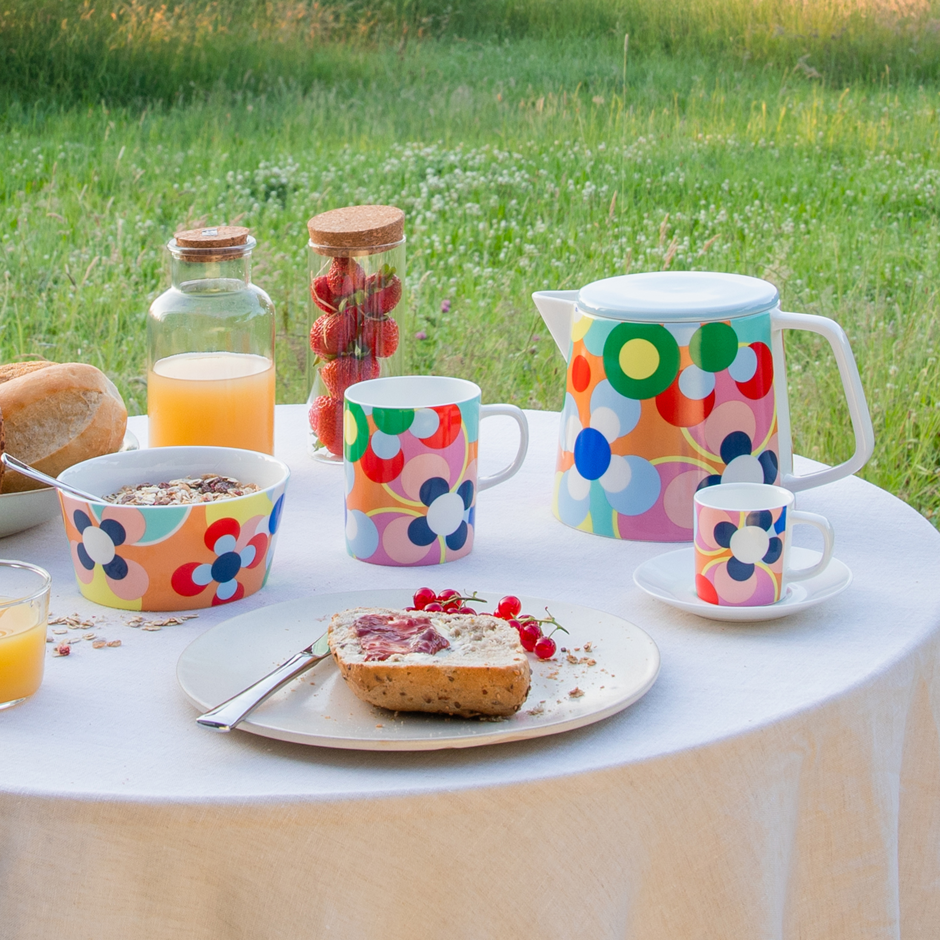 Breakfast in the countryside: table with muesli, juice, strawberries, bread with jam and colourful crockery with a floral pattern. The jug, cups and bowl are ready and waiting.