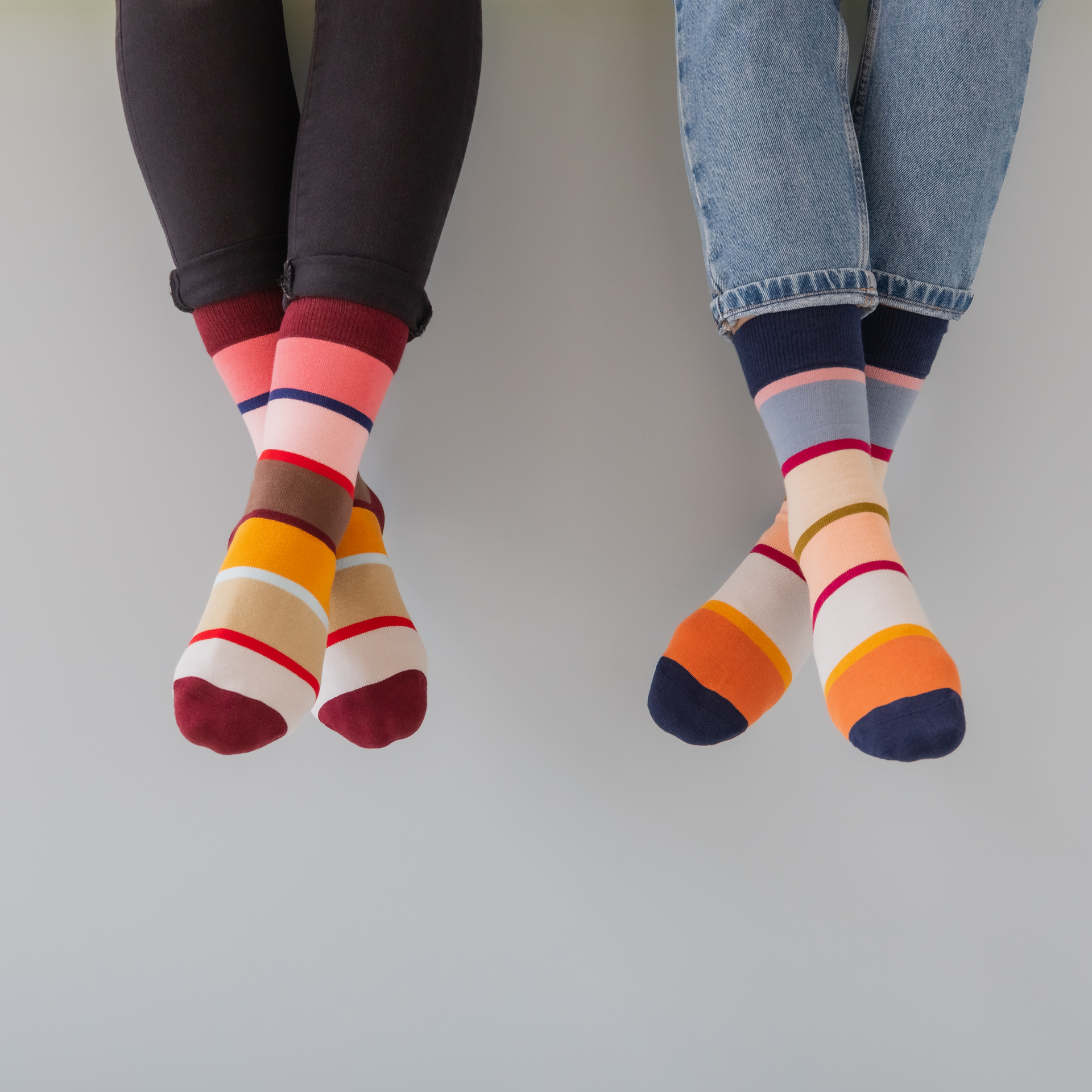 Zwei farbenfrohe Herrensocken mit Streifenmuster in Orange, Weiß, Lila, Blau und Rosa. Dunkelblaue Bündchen und verstärkte Fersen.