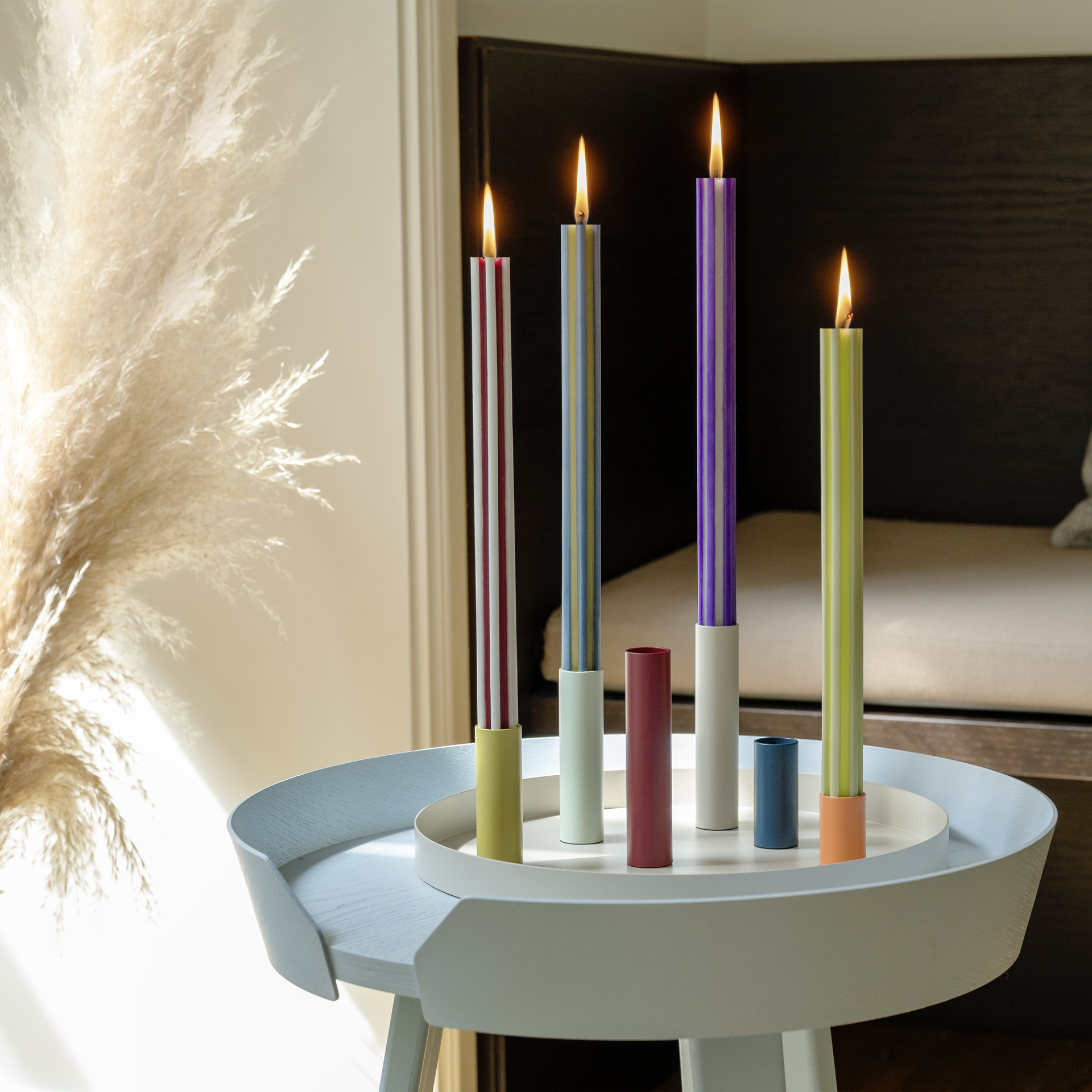 Una bandeja con seis candelabros de colores, dos de ellos con velas de color verde claro, en azul, naranja, amarillo, rojo, verde claro y beige.