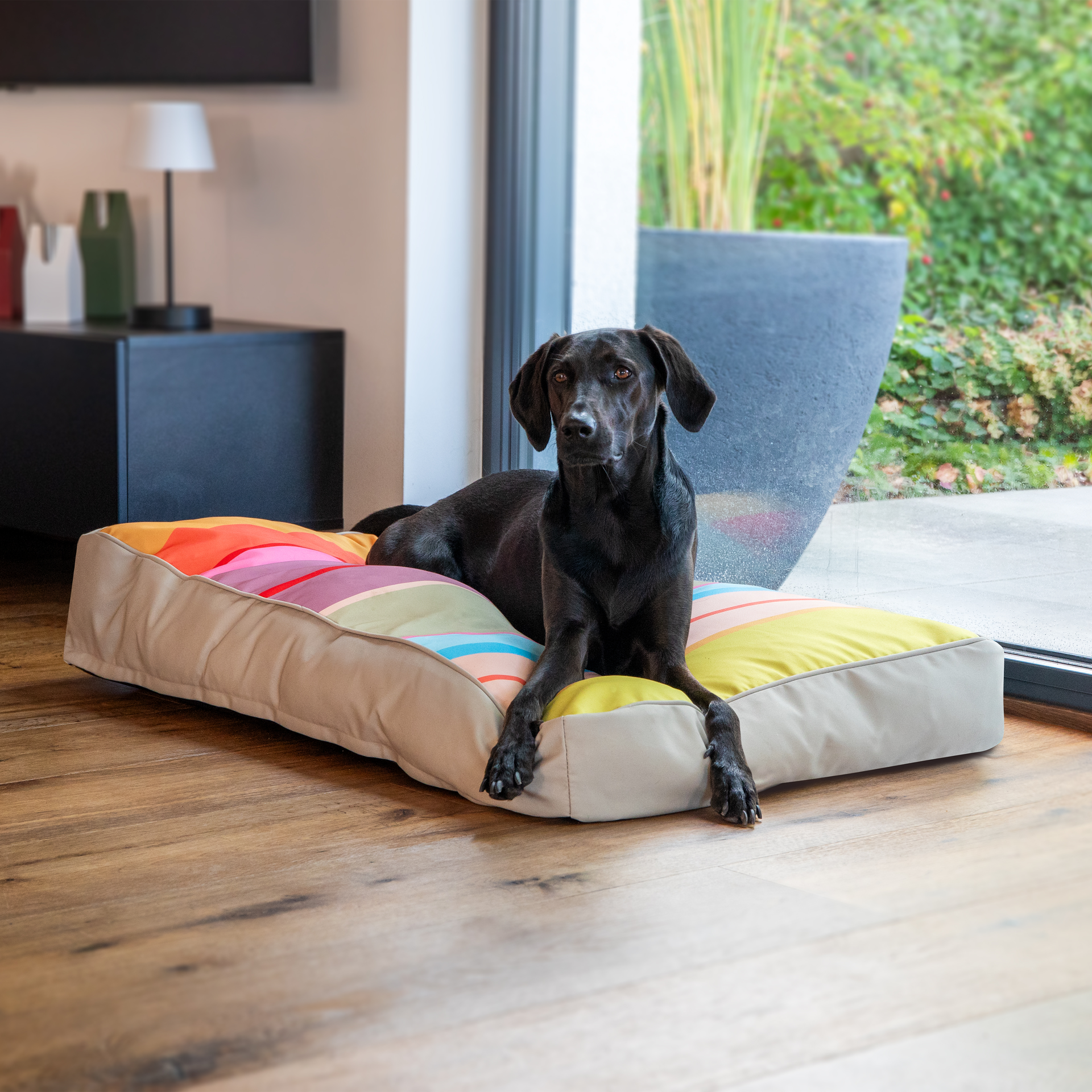 Rechteckiges Hundekissen Theo in Größe L mit robustem, beigefarbenem Unterteil und auffälliger, bunter Oberseite. Breite, horizontale Streifen in Gelb, Orange, Rot, Rosa, Lila, Grün und Hellblau bieten einen bequemen Liegeplatz.