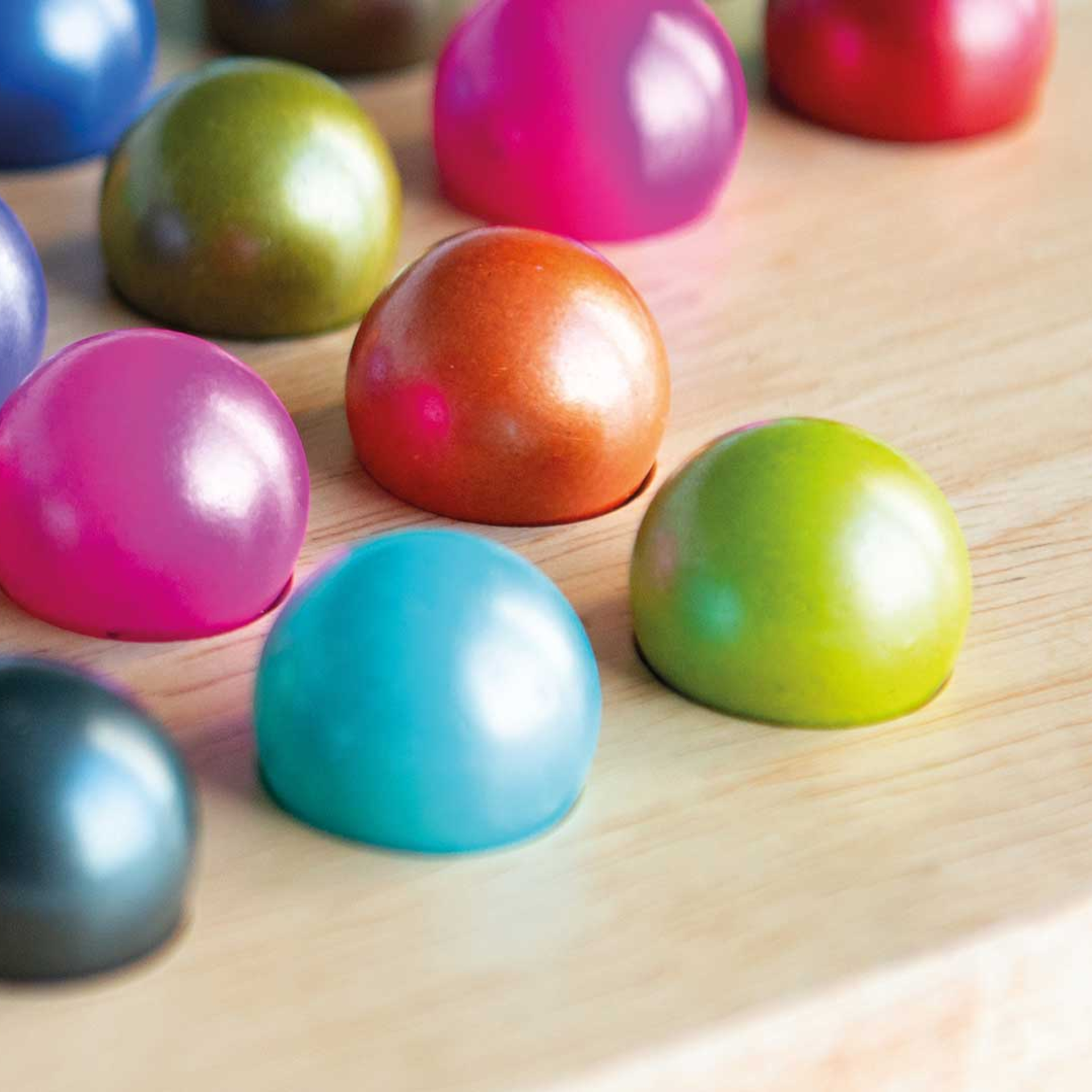 Close-up of coloured glass balls on a light wooden board, part of the solitaire game. Balls in blue, green, pink, red and brown.