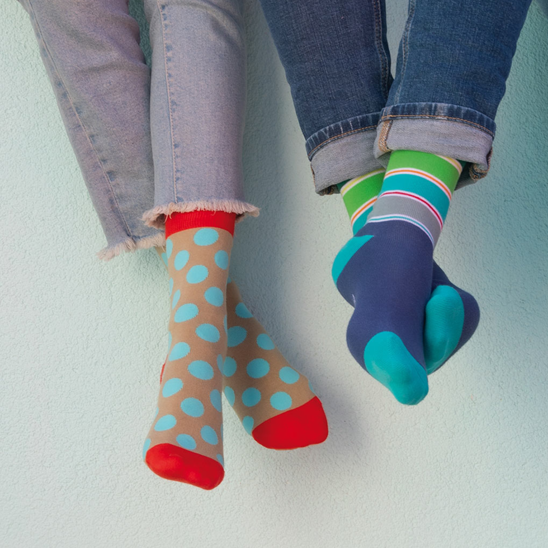Deux paires de pieds avec des chaussettes colorées. Une paire avec des chaussettes marron clair et des pois bleus. L'autre paire avec des chaussettes rayées en vert, turquoise et gris.