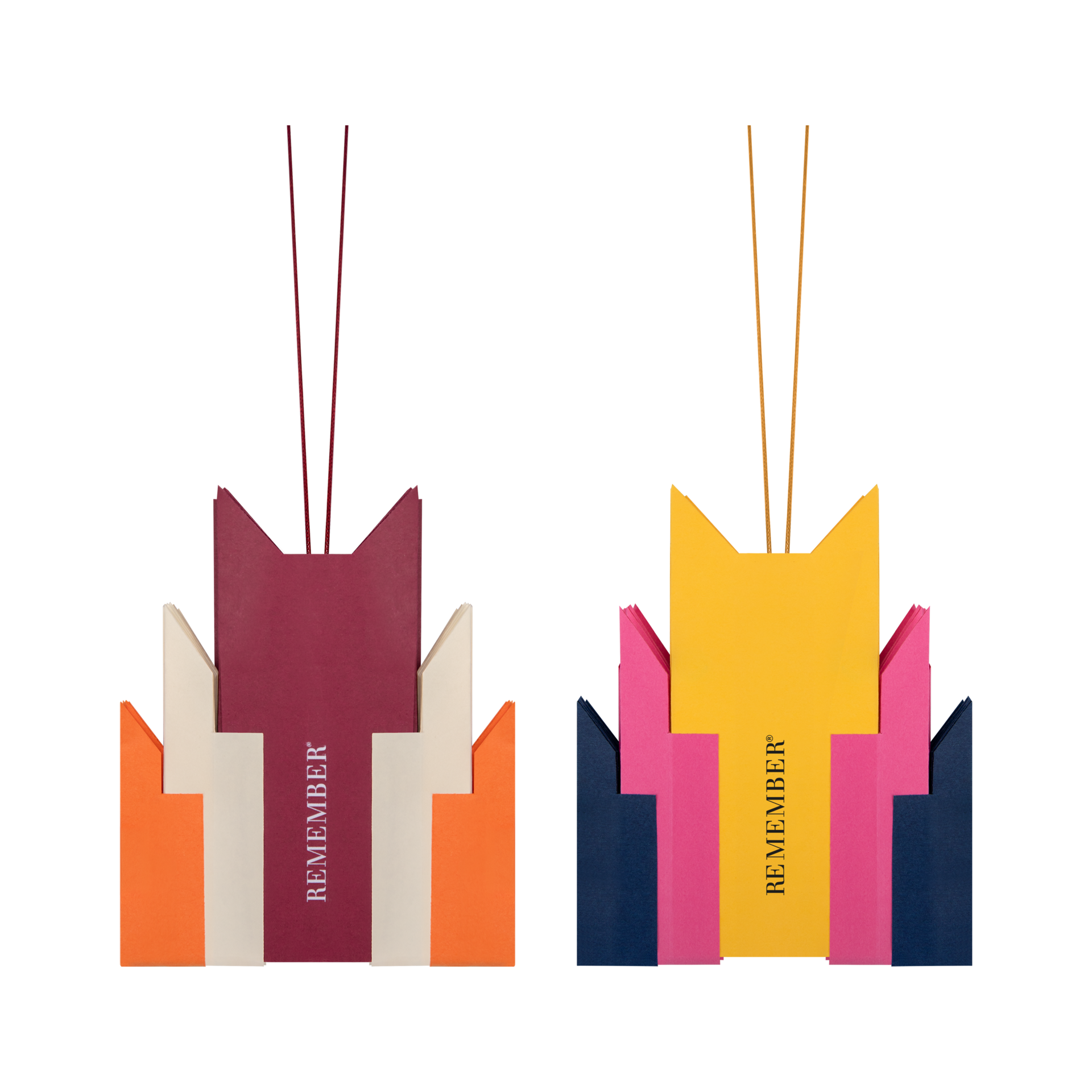 Dos coloridas estrellas de papel plegadas con diseño Nova sobre fondo blanco. A la izquierda, en color burdeos, beige y naranja; a la derecha, en amarillo brillante, rosa y azul marino. Con finos cordones y la inscripción « REMEMBER ».