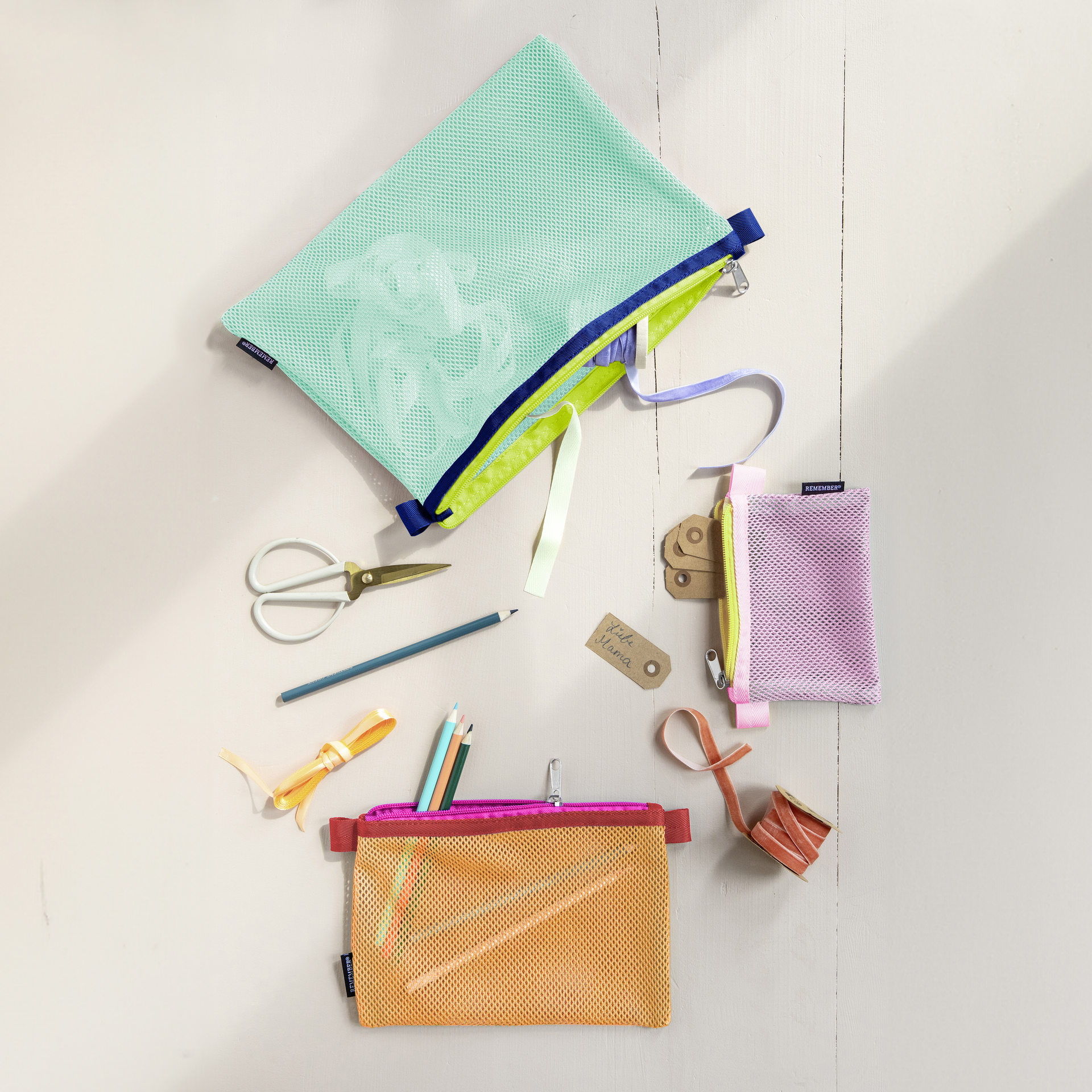 Bolsitas de malla de varios colores, lápices, tijeras, cintas de regalo y una etiqueta con la inscripción «Querida mamá» sobre un fondo claro.