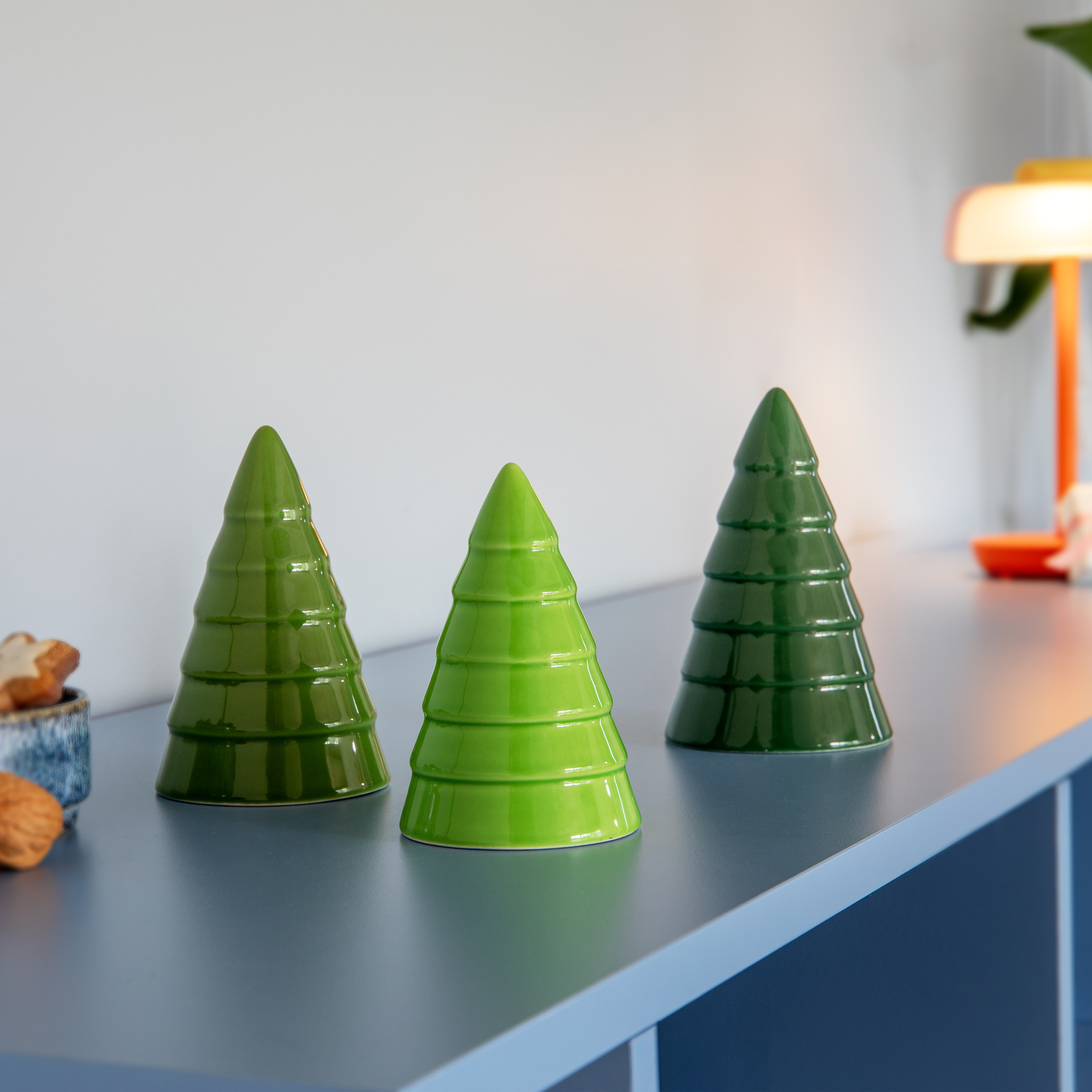 Três árvores decorativas em cerâmica em forma de abetos sobre fundo branco. Da esquerda para a direita: verde escuro, verde médio, verde claro. Esmaltadas com acabamento brilhante e ranhuras horizontais e textura em camadas.