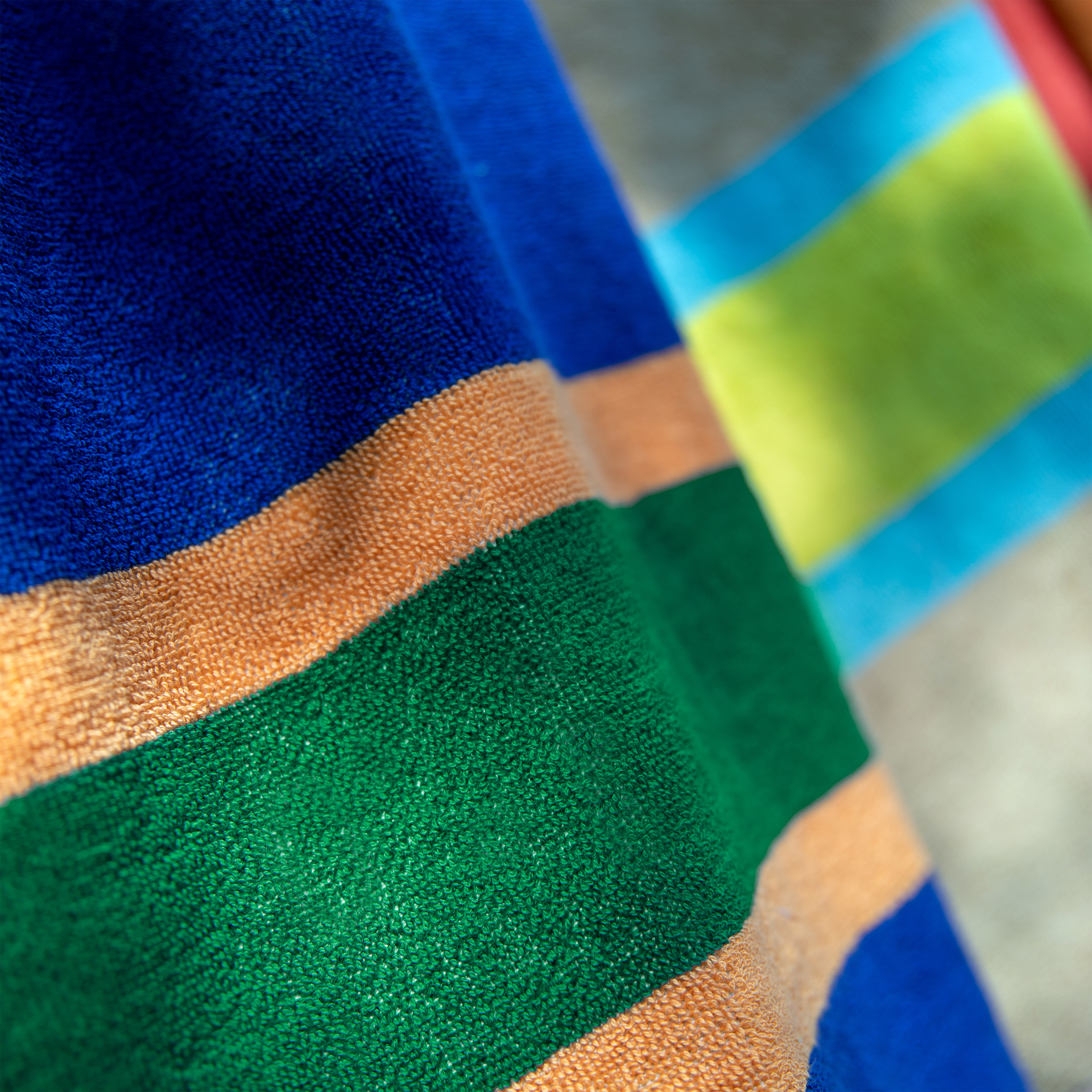 Gros plan sur la serviette de bain moelleuse « Tallinn », ornée de larges rayures colorées en bleu foncé, orange vif et vert intense. La texture en coton éponge souligne le pouvoir absorbant et la douceur de cette serviette extra-large.