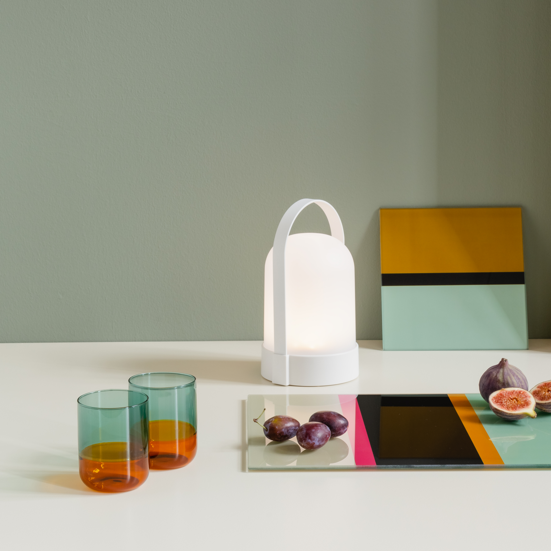 Two 'amber' glasses, a lamp and fruit on a table. The glasses are two-coloured, blue at the top and amber at the bottom.