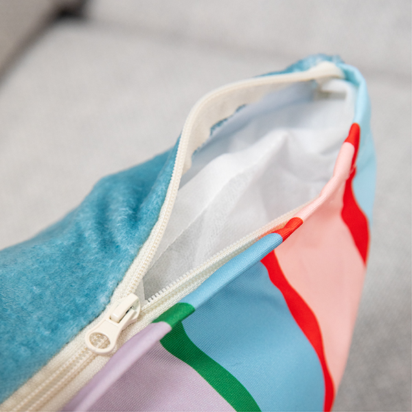 Close-up of an open, beige zip on a cushion cover. One section is fluffy and turquoise-blue, the other is striped in light blue, pink, red, green and lavender. White inner lining visible.