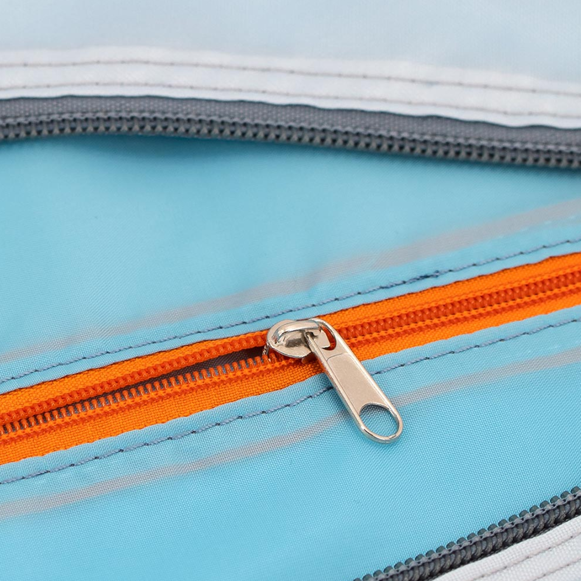 Primo piano di una borsa da viaggio e tempo libero "Tom" aperta, con cerniera arancione e fodera azzurra. La chiusura lampo è in metallo.