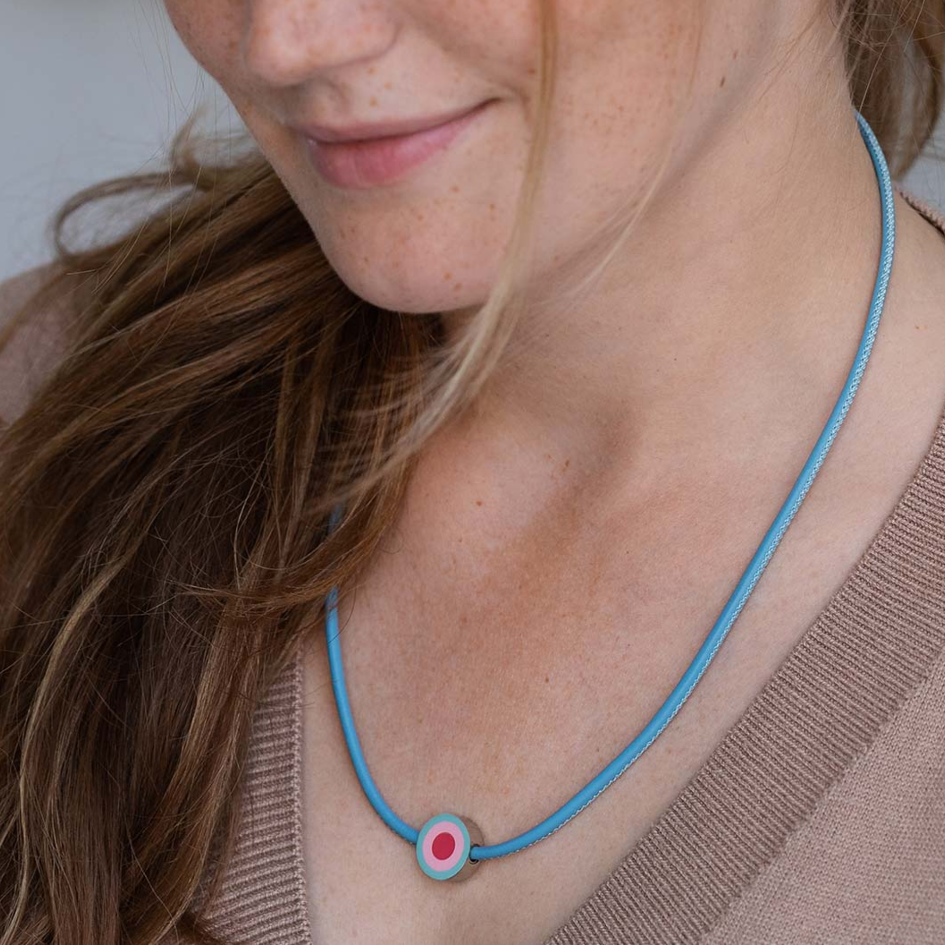 Primo piano di una donna con un ciondolo su una collana turchese. Il ciondolo rotondo ha un punto rosso al centro, circondato da un cerchio rosa.