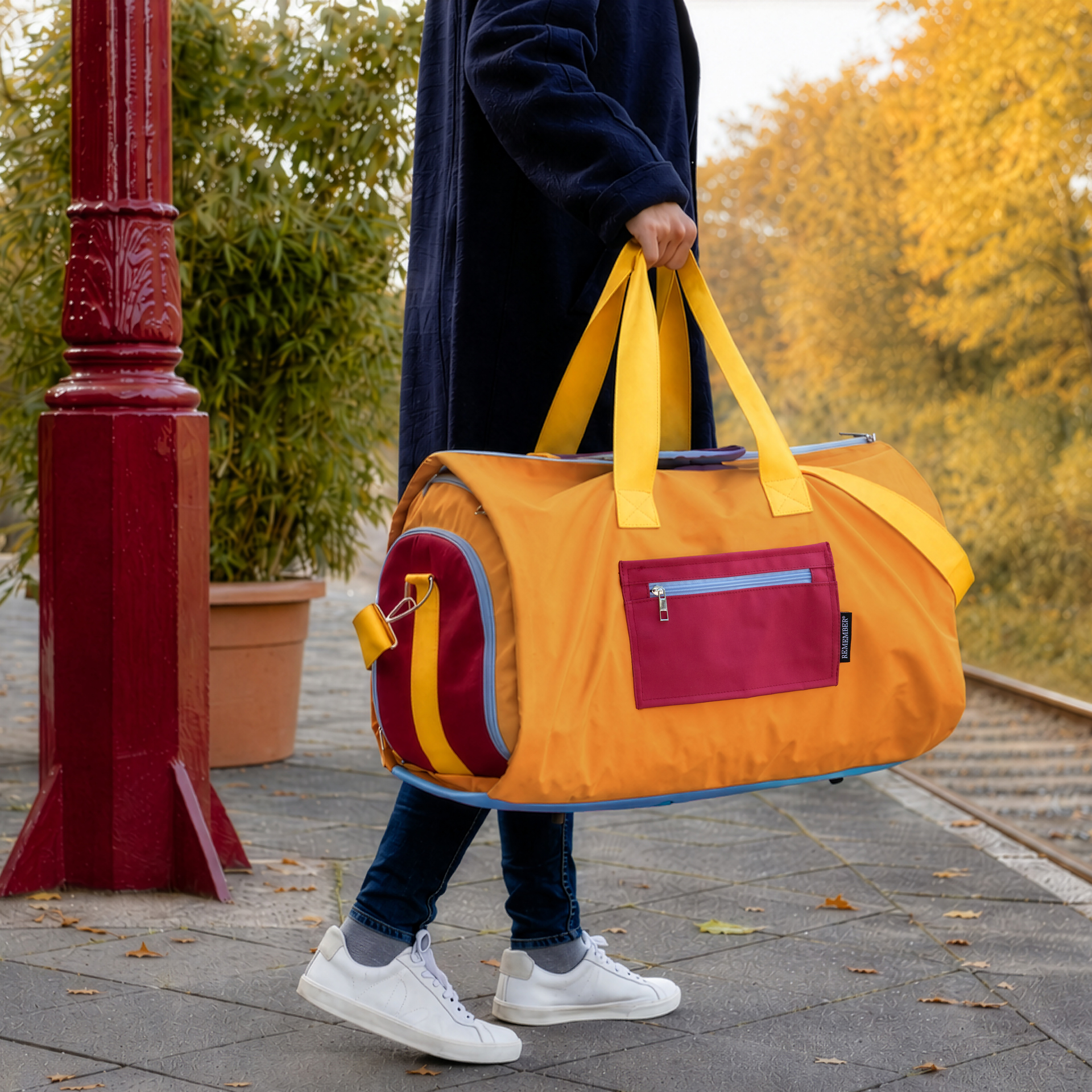 Orangefarbene Reisetasche Lennard Pumpkin mit gelben Tragegurten und bordeauxrotem, gepolstertem Schultergurt. Hellblaue Reißverschlussakzente und bordeauxrote Endpartien betonen das Design. Aus wasserabweisendem Material.