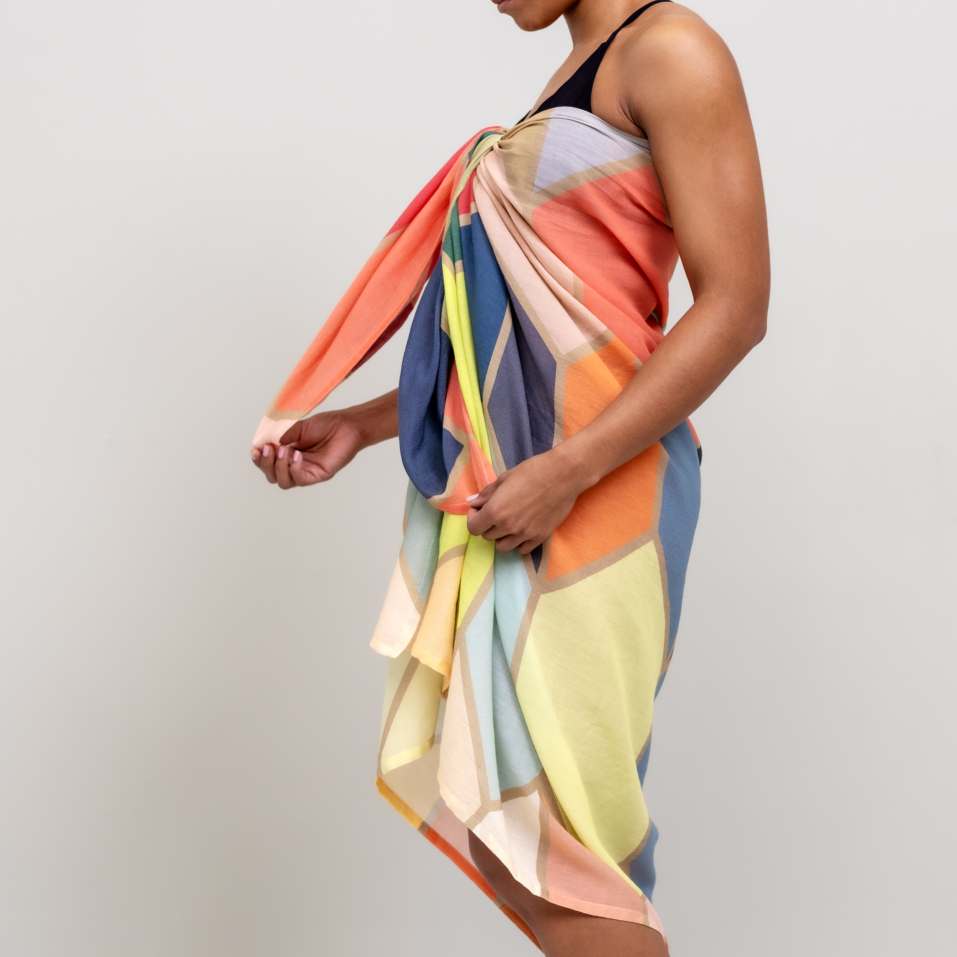 Una persona lleva el pareo «Waikiki», envuelto alrededor del cuerpo. El paño presenta un estampado geométrico en naranja, azul, amarillo y gris.