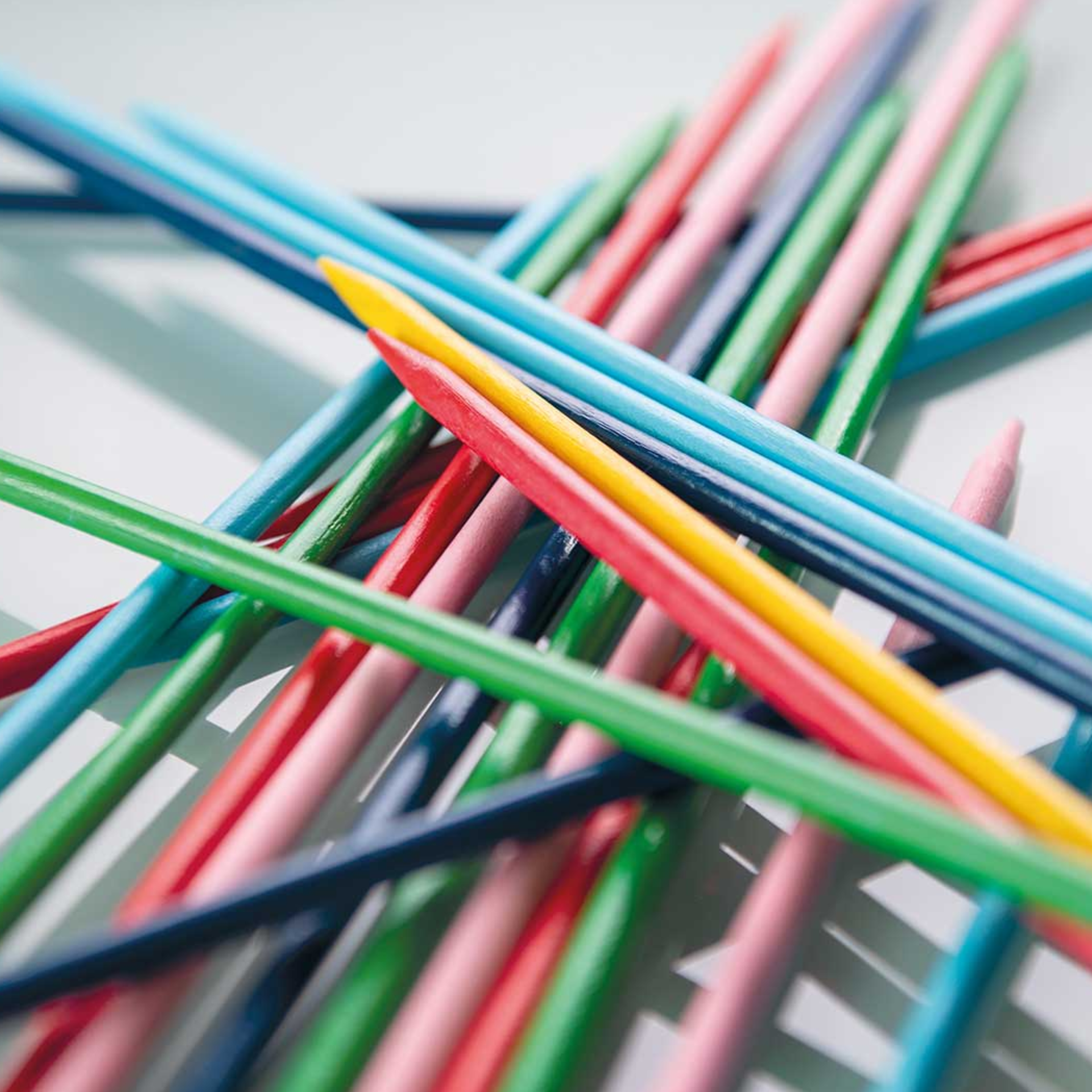 Close-up van gekruiste, kleurrijke houten stokjes van het spel Stickado. De stokjes zijn rood, geel, groen, blauw en roze gekleurd.