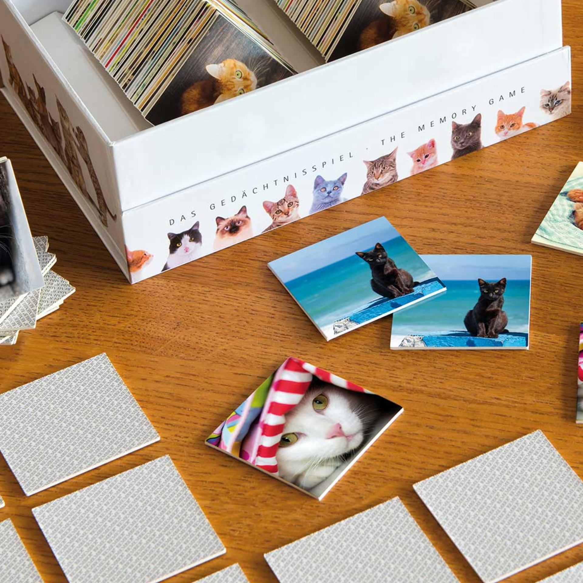 Weiße Verpackung des 'Remember Cats' Spiels, mit einer schwarz-weißen Katze auf der Oberseite. Der Schriftzug "Remember" ist groß abgebildet. An den Seiten sind Katzenfotos zu sehen.
