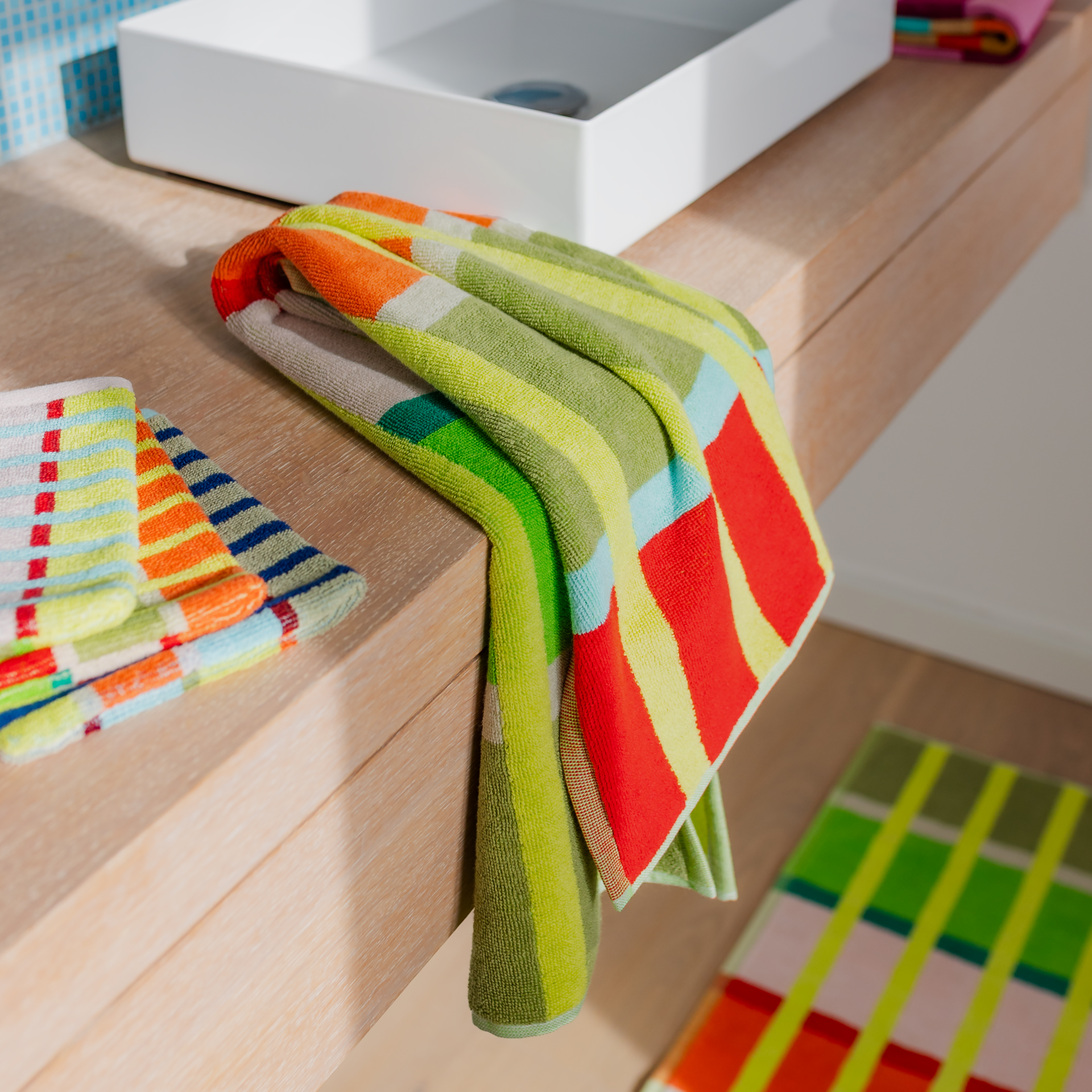 Toalla Kaido plegada con un alegre estampado a cuadros: rayas amarillas verticales y franjas horizontales en colores vivos. Los tonos marrón grisáceo, blanco, verde, rosa, coral, azul claro y rojo le dan a esta toalla de algodón un aspecto alegre.
