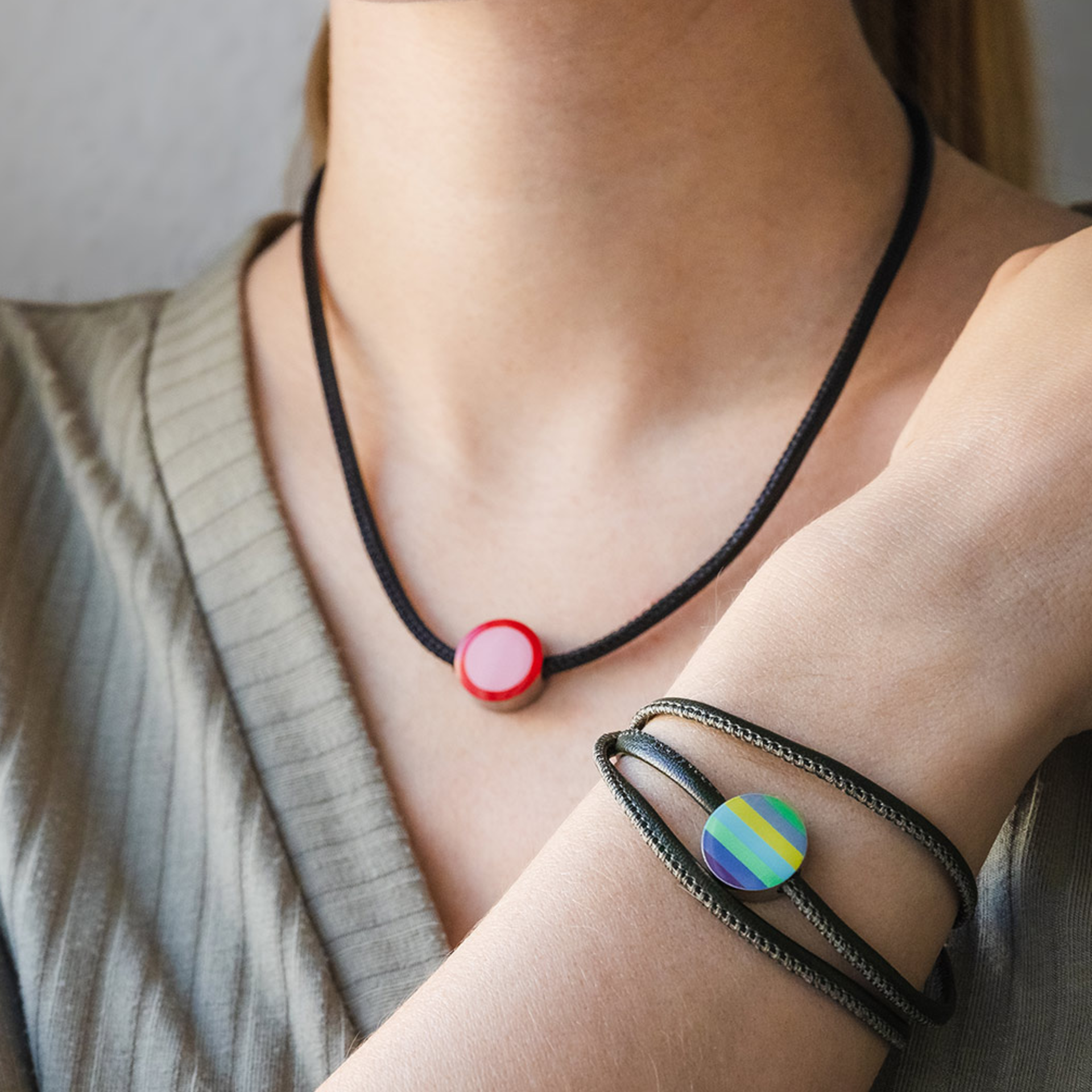 Primo piano di collana e bracciale con ciondoli rotondi a strisce rosa e multicolore. Entrambi i gioielli sono dotati di nastri neri.
