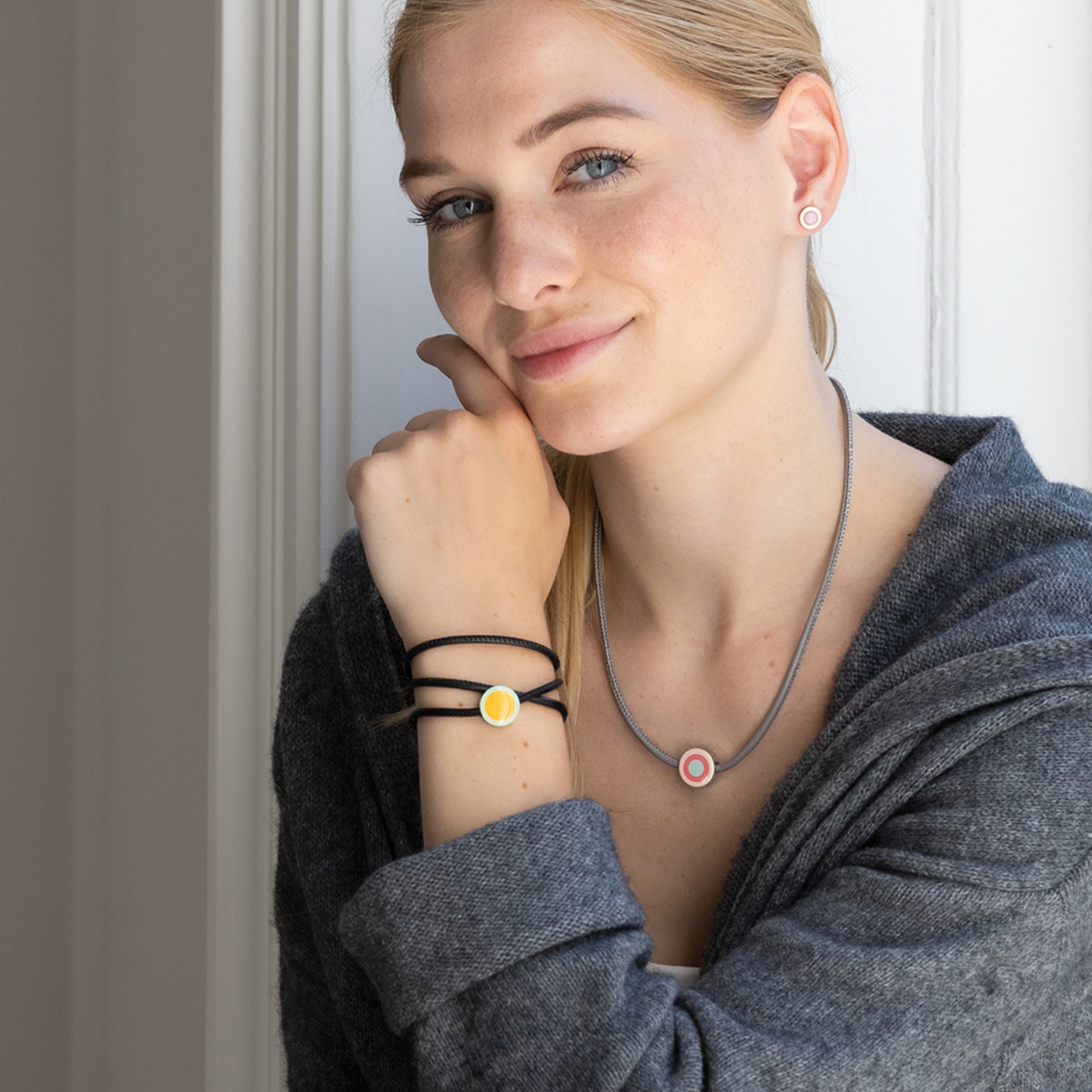 Frau mit Schmuck Anhänger und passendem Armband. Halskette und Ohrringe in Rosa, Armband mit gelbem Anhänger.