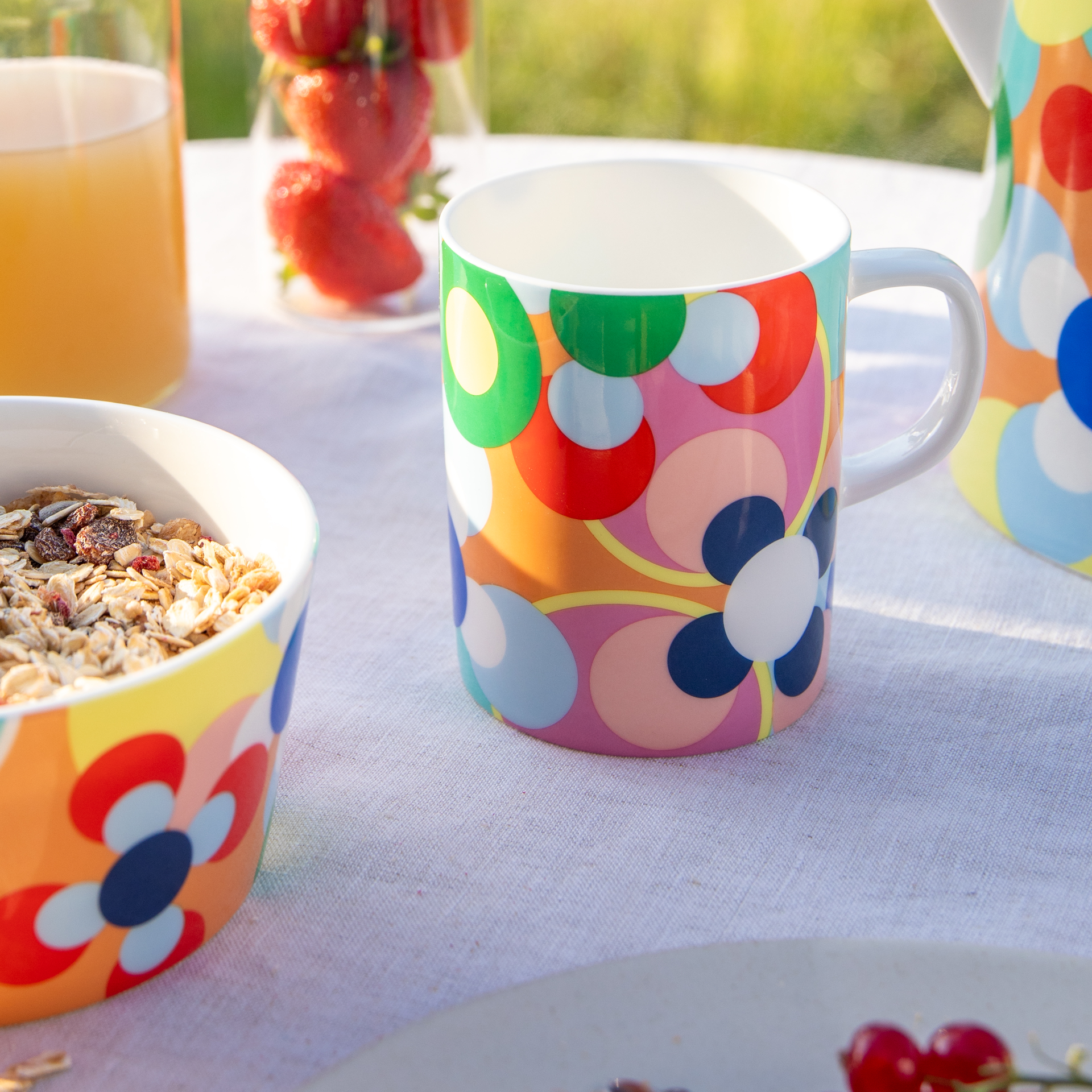 A porcelain cup with handle, decorated with a colourful circle pattern in yellow, green, red, pink and blue.