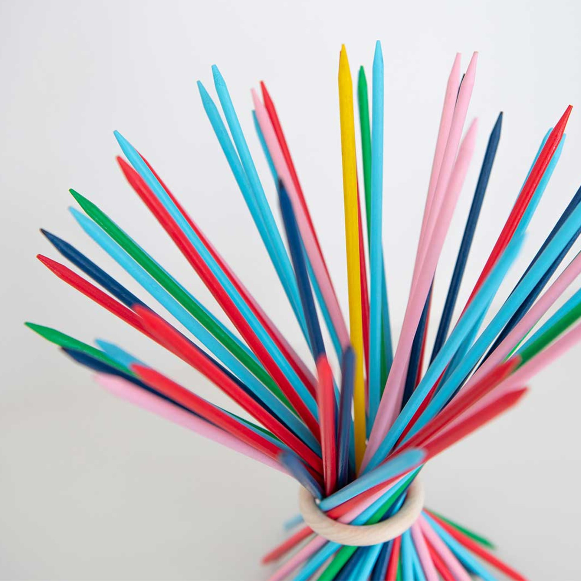 Close-up van kleurrijke Stickado houten stokjes die bij elkaar worden gehouden door een lichtgekleurde houten ring. De stokjes zijn in verschillende kleuren geverfd.