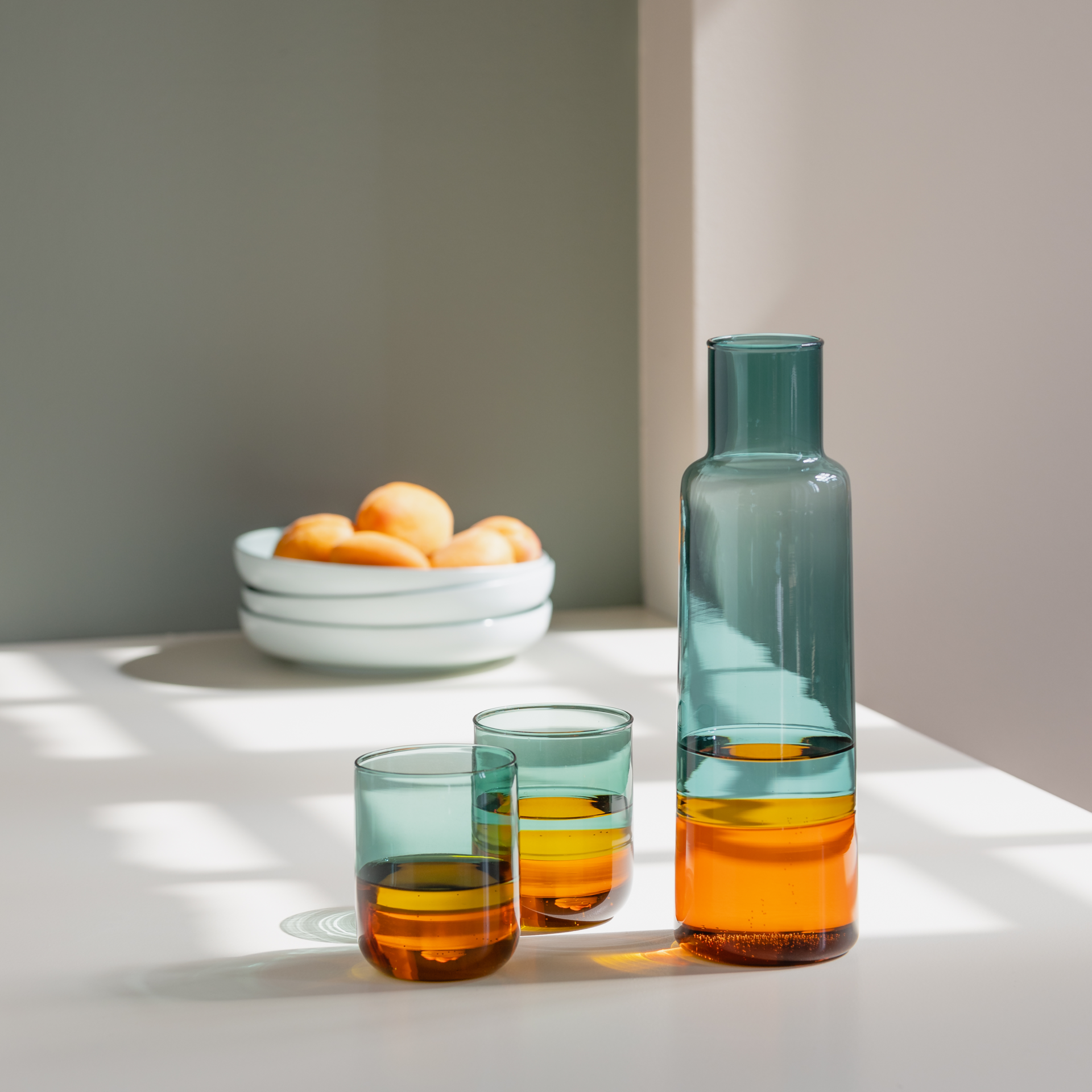 Caraffa di vetro alta e sottile. La parte superiore è verde, quella inferiore ambrata. Le transizioni sono senza soluzione di continuità. Contenitore di vetro trasparente e vuoto.