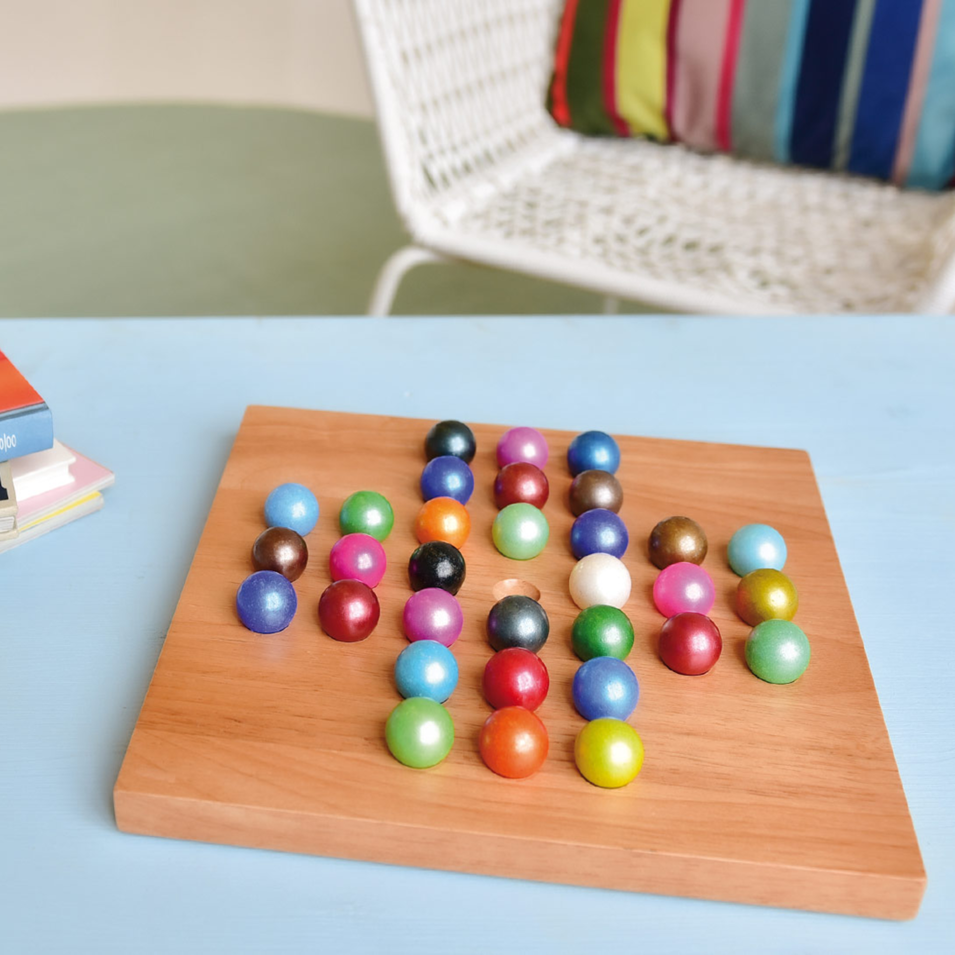 Wooden board with coloured glass balls in a solitaire pattern. In the background is a chair and a cushion.