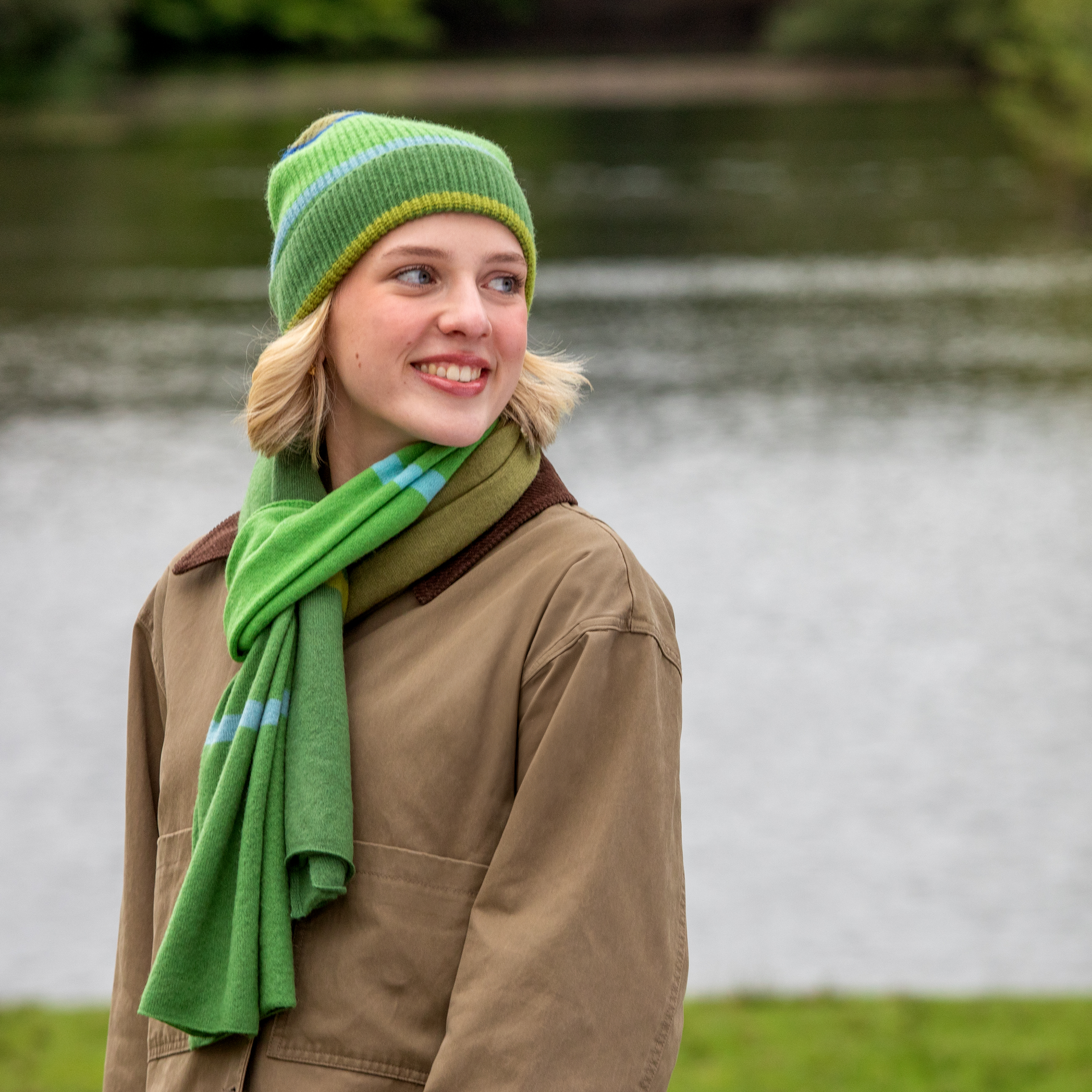 Sciarpa in lana cashmere verde a righe blu e gialle, drappeggiata e fluttuante su sfondo bianco.