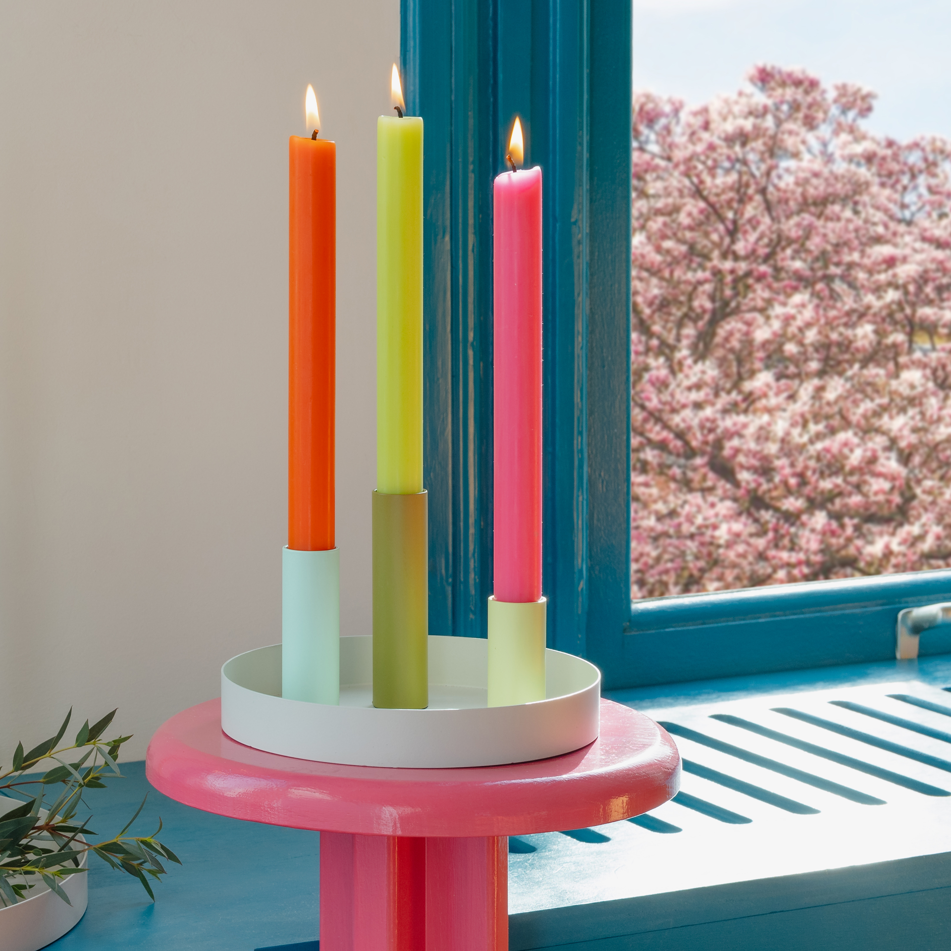 Portavelas Luna Mini: bandeja gris con tres soportes de colores en tonos verdes y azules; dos soportes sostienen velas largas de color verde claro.