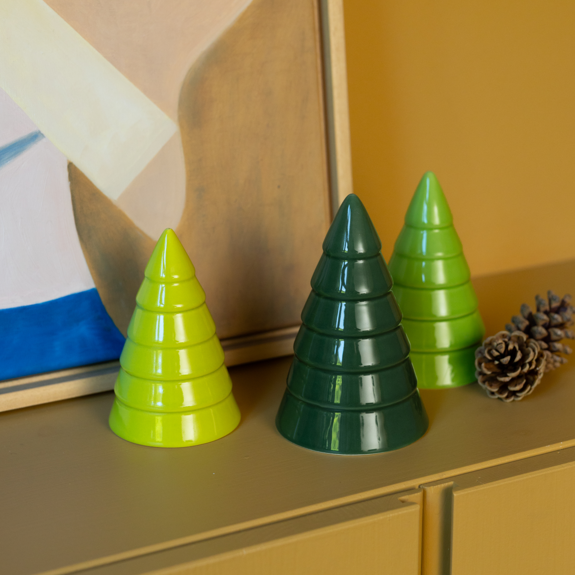 Tres árboles decorativos de cerámica con forma de abeto sobre fondo blanco. De izquierda a derecha: verde oscuro, verde medio, verde claro. Esmaltados con acabado brillante y ranuras horizontales que representan ramas estilizadas y una textura en capas.
