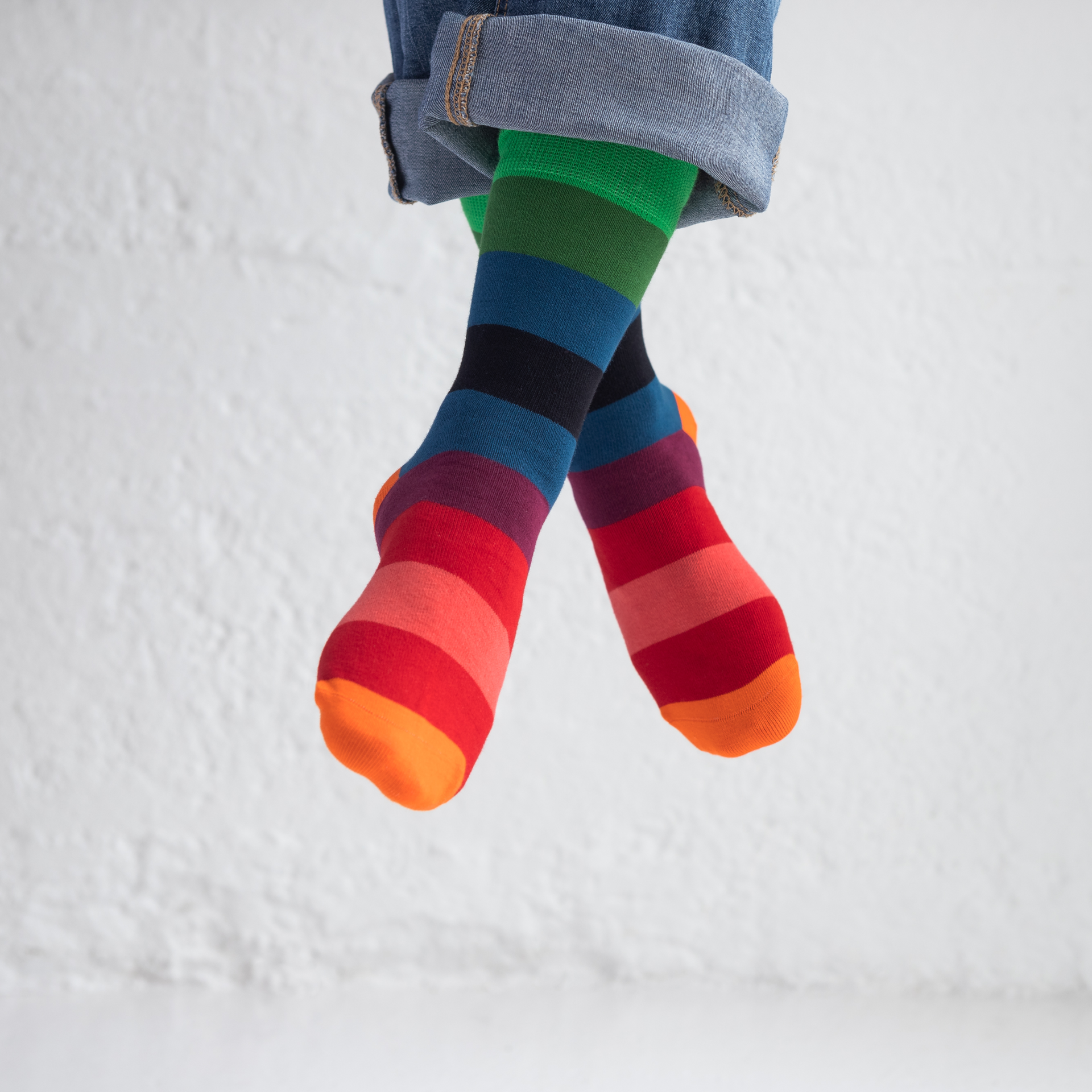 Benen met opgerolde jeans en kleurrijke, gestreepte sokken, maat 36-41, tegen een witte achtergrond.