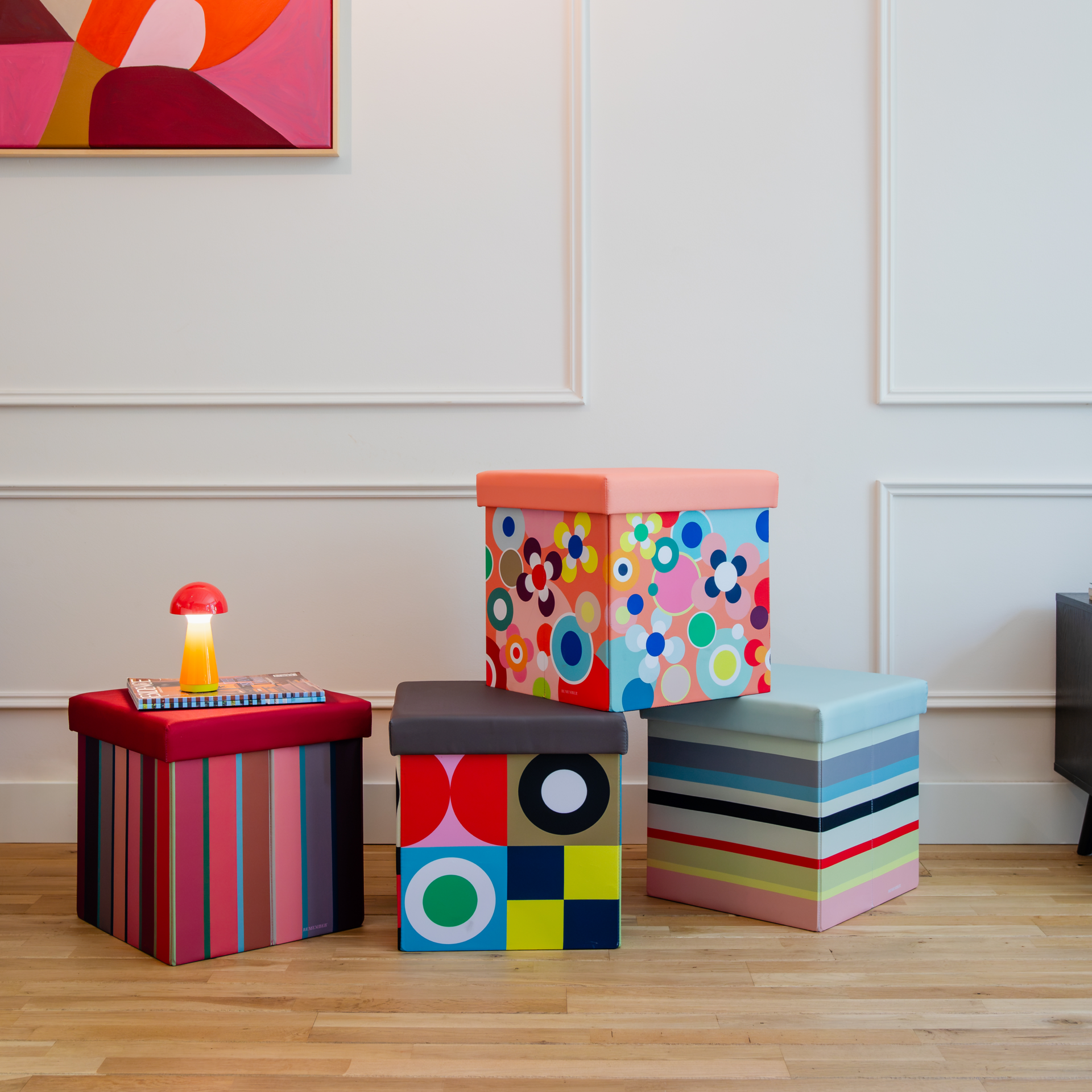 Vier farbenfrohe Sitzboxen stehen auf einem Holzboden. Die Remember Boxen zeigen Streifen sowie florale und geometrische Muster. Sie dienen als Sitzgelegenheiten und bieten praktischen Stauraum.