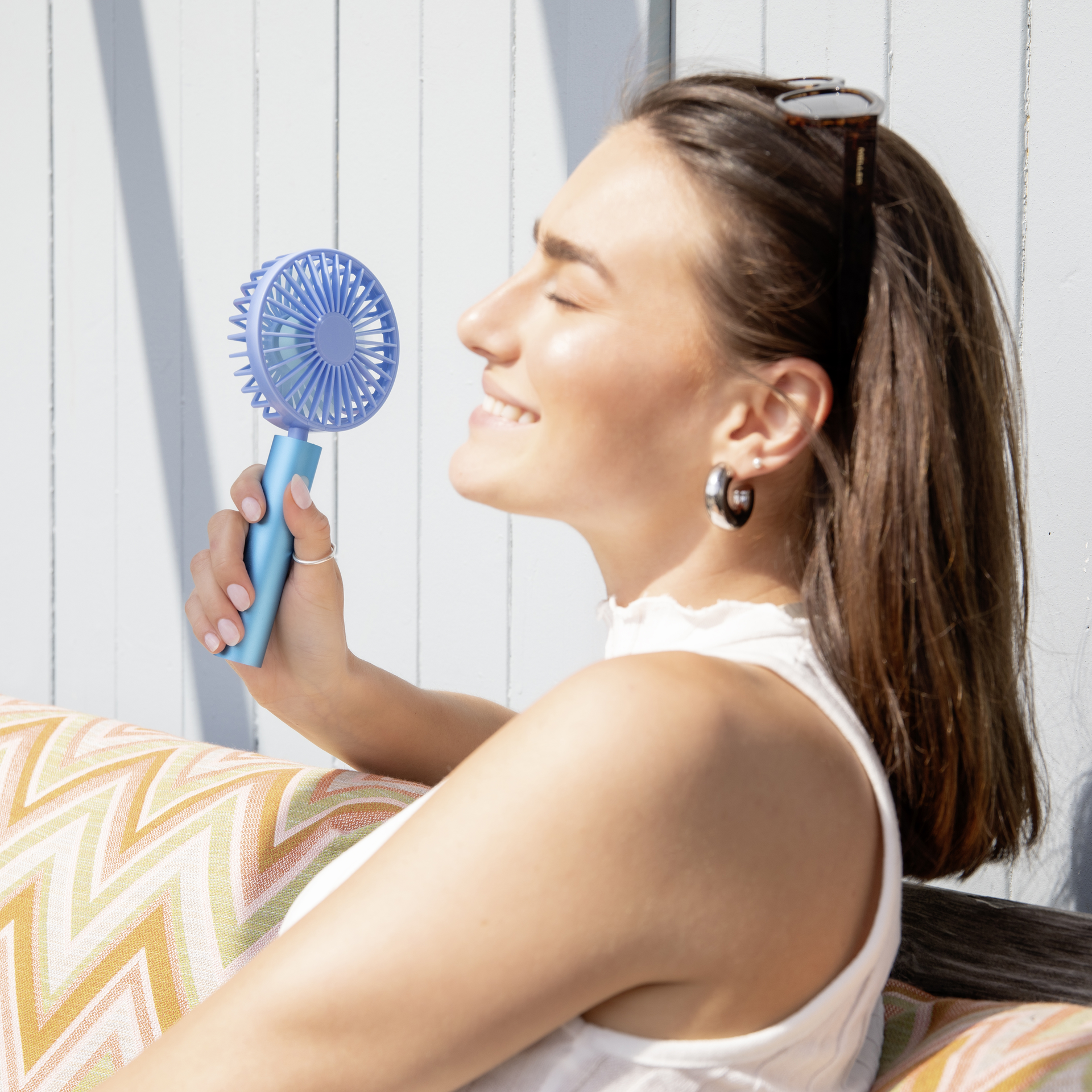 Ein aqua-farbener, tragbarer Ventilator mit schwenkbarem Kopf und einem runden Gitter, das die Rotorblätter schützt. Der Griff ist zylindrisch mit einem Knopf.