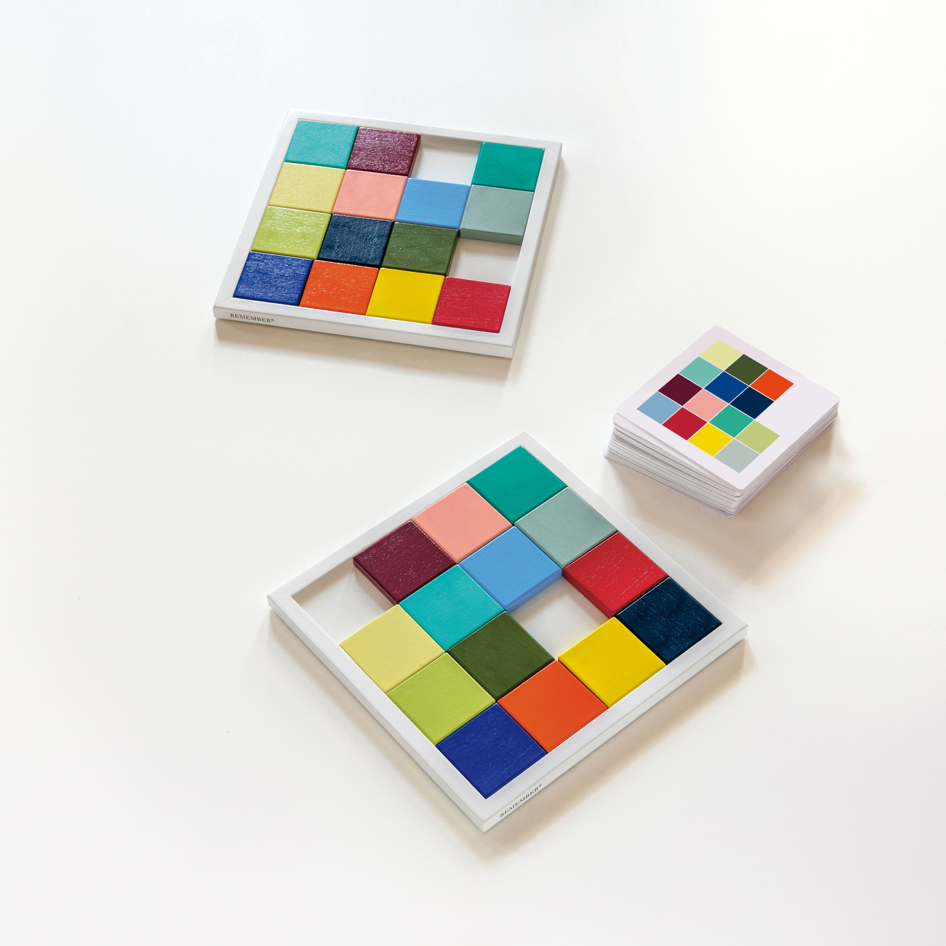 Dos tableros de juego «SKUBBE» con fichas de madera de colores y una baraja de cartas sobre un fondo blanco.