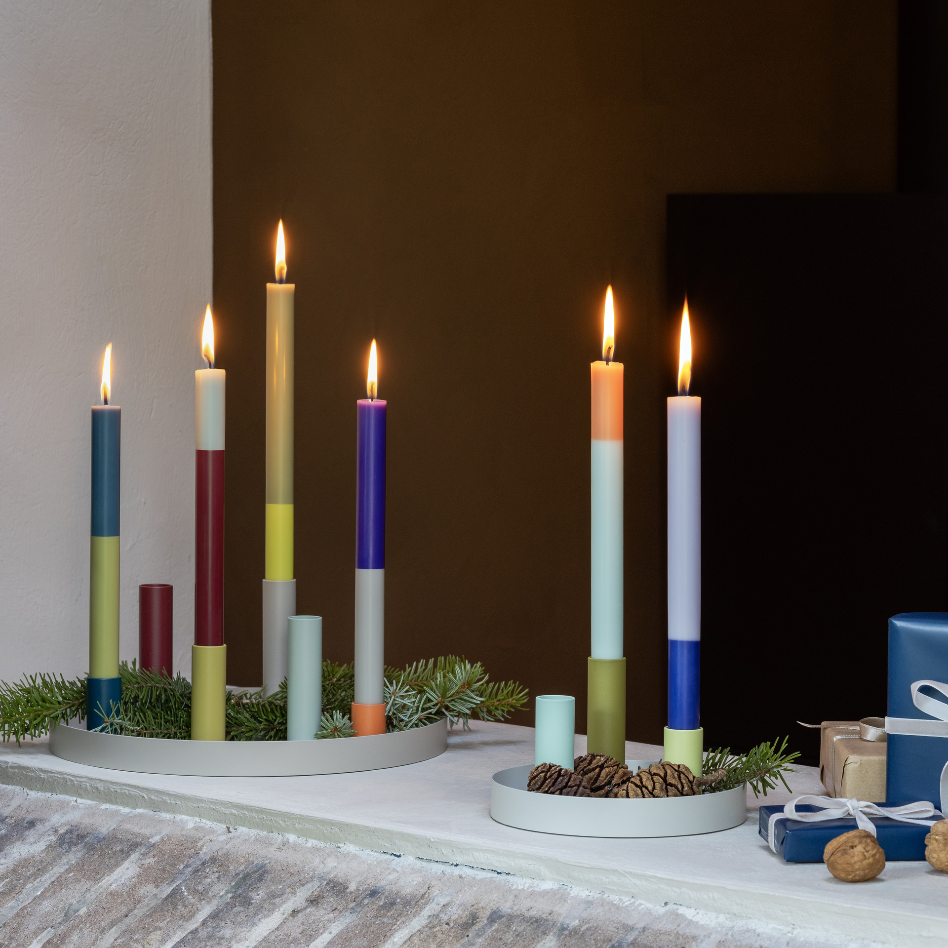 Due vassoi grigi con portacandele magnetici di diversi colori e candele accese. Decorare con rami di abete, pigne e regali.