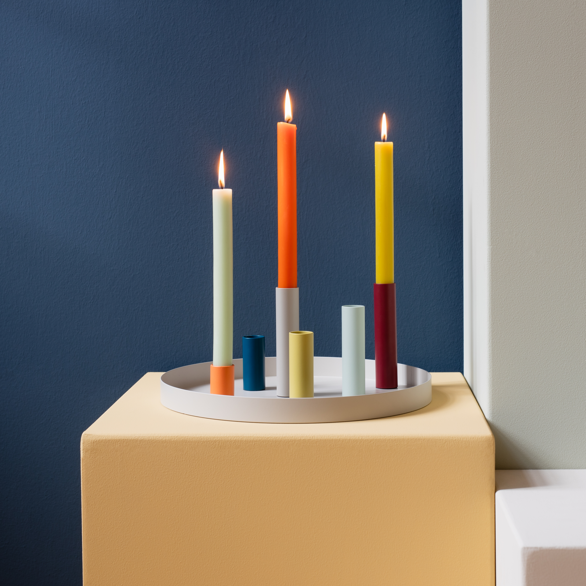 Composizione del portacandele magnetico "Luna" con candele colorate su un vassoio davanti a una parete blu. Tre candele sono accese.