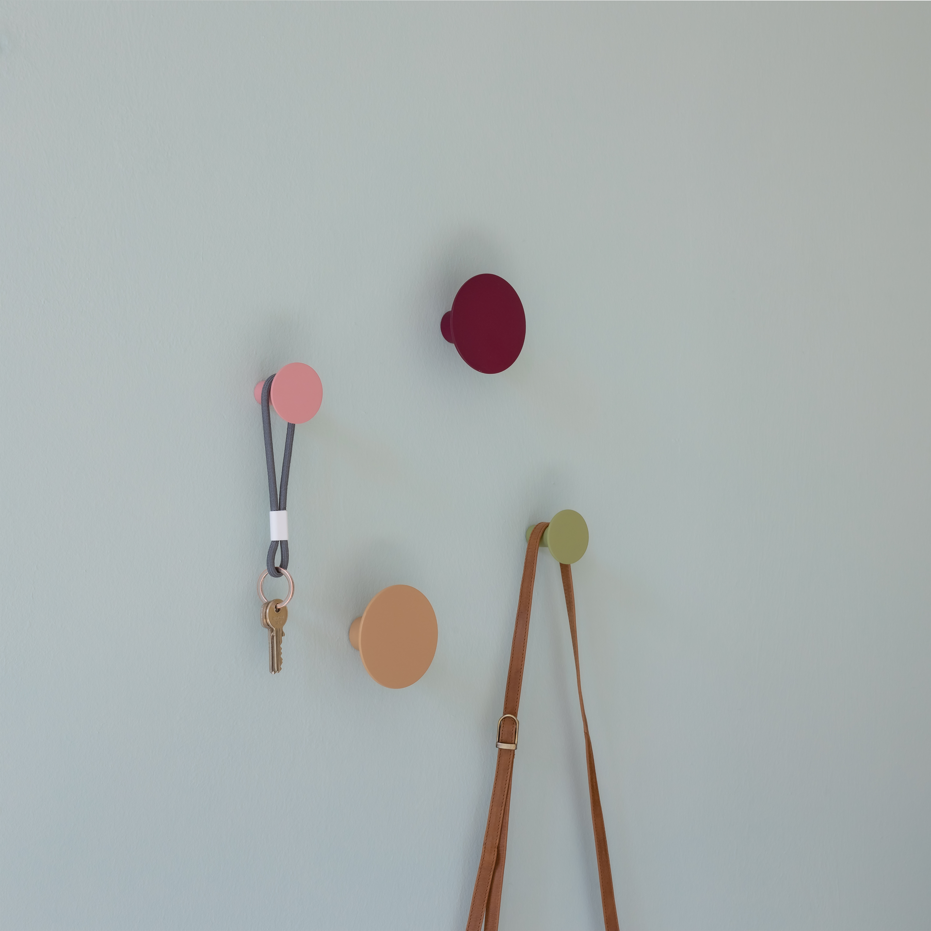 Set de crochets muraux multicolores : deux grands crochets en beige et bordeaux, deux petits crochets en rose et vert menthe sur fond blanc.
