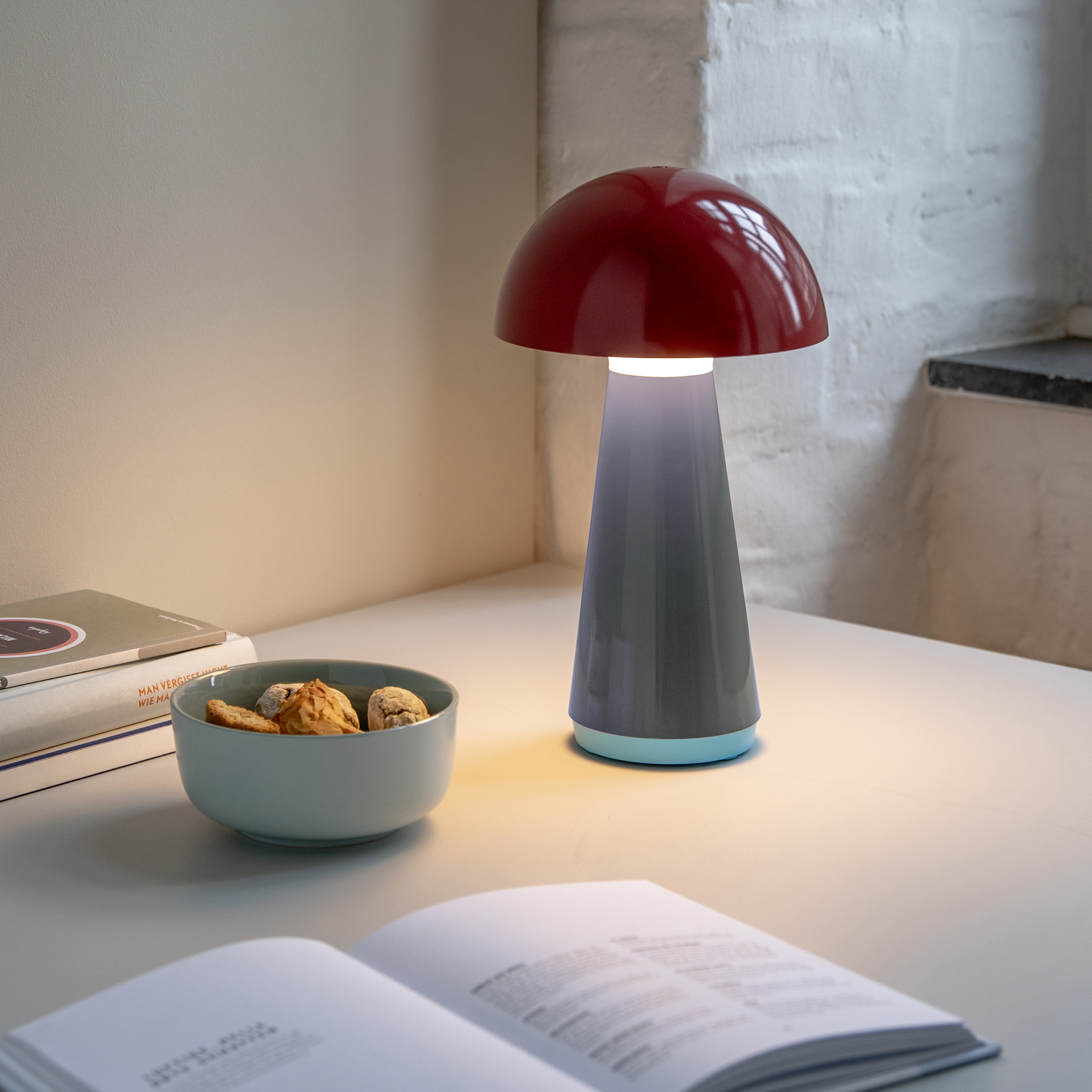 Lámpara de mesa roja «Bob» con diseño de seta. La pantalla es roja, el cuello gris y la base azul claro. La lámpara aparece aislada sobre un fondo blanco.